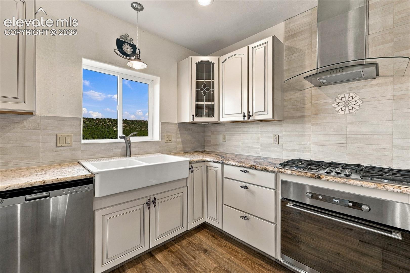 Kitchen featuring white cabinetry with glass-panel accents, stone-finish countertops, an apron-front sink, stainless steel appliances, and horizontal tiled backsplash