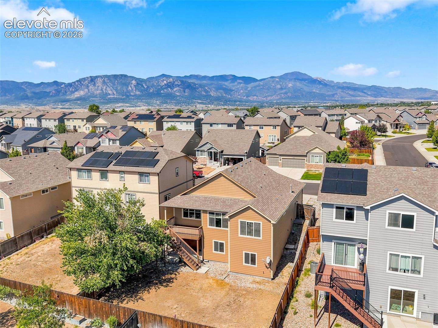 Residential neighborhood with a mountain backdrop, featuring solar panels on multiple rooftops, and various house styles