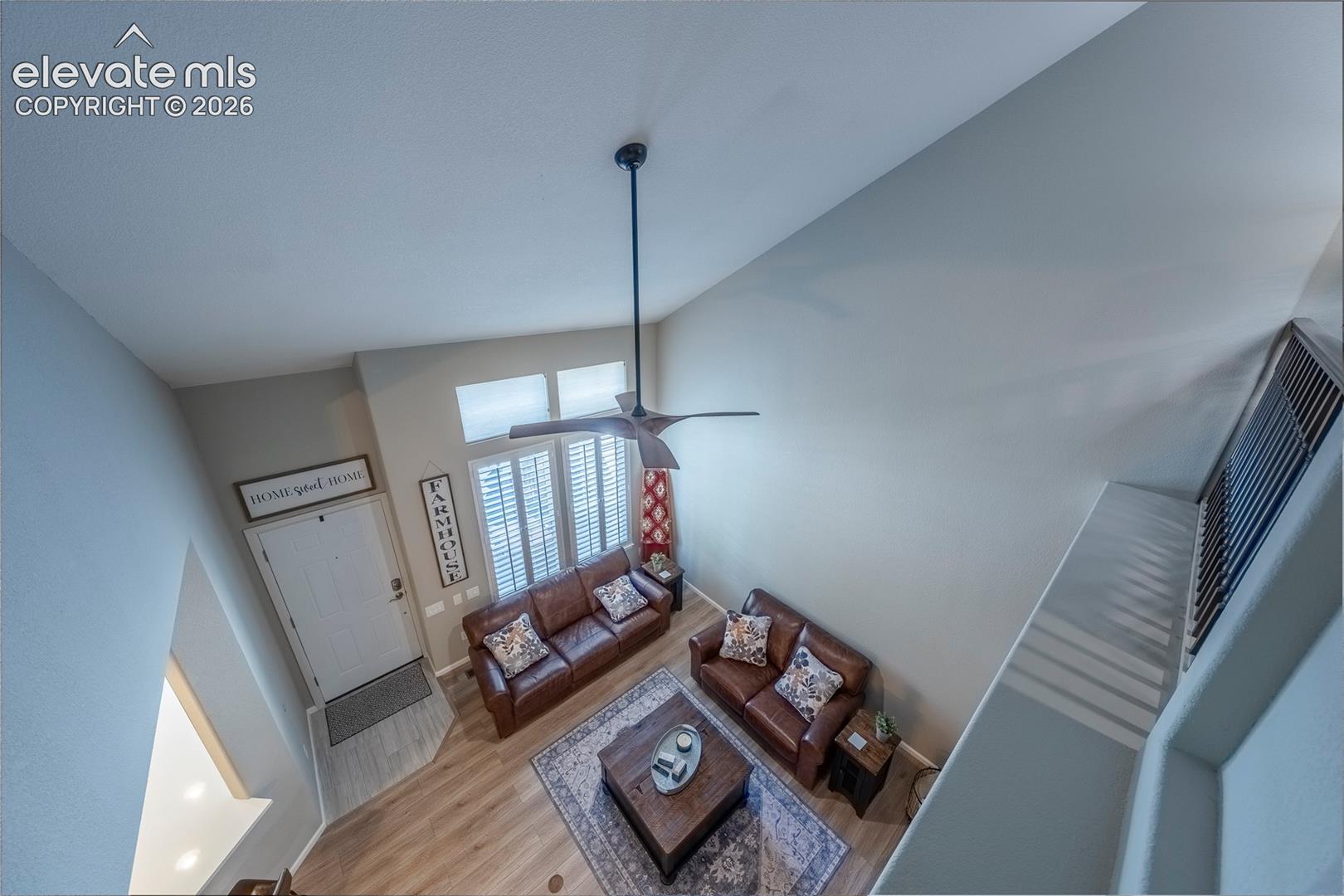 High-ceiling interior featuring wood-finish flooring, multi-pane windows with integrated shutters, and a ceiling fan with an extended downrod