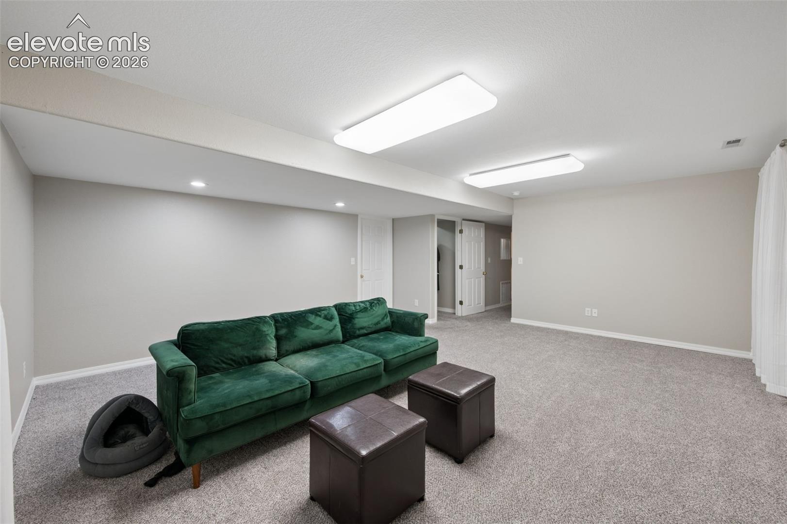 Neutral-toned interior space featuring wall-to-wall carpeting, recessed ceiling lighting, and dual flush-mount rectangular light fixtures