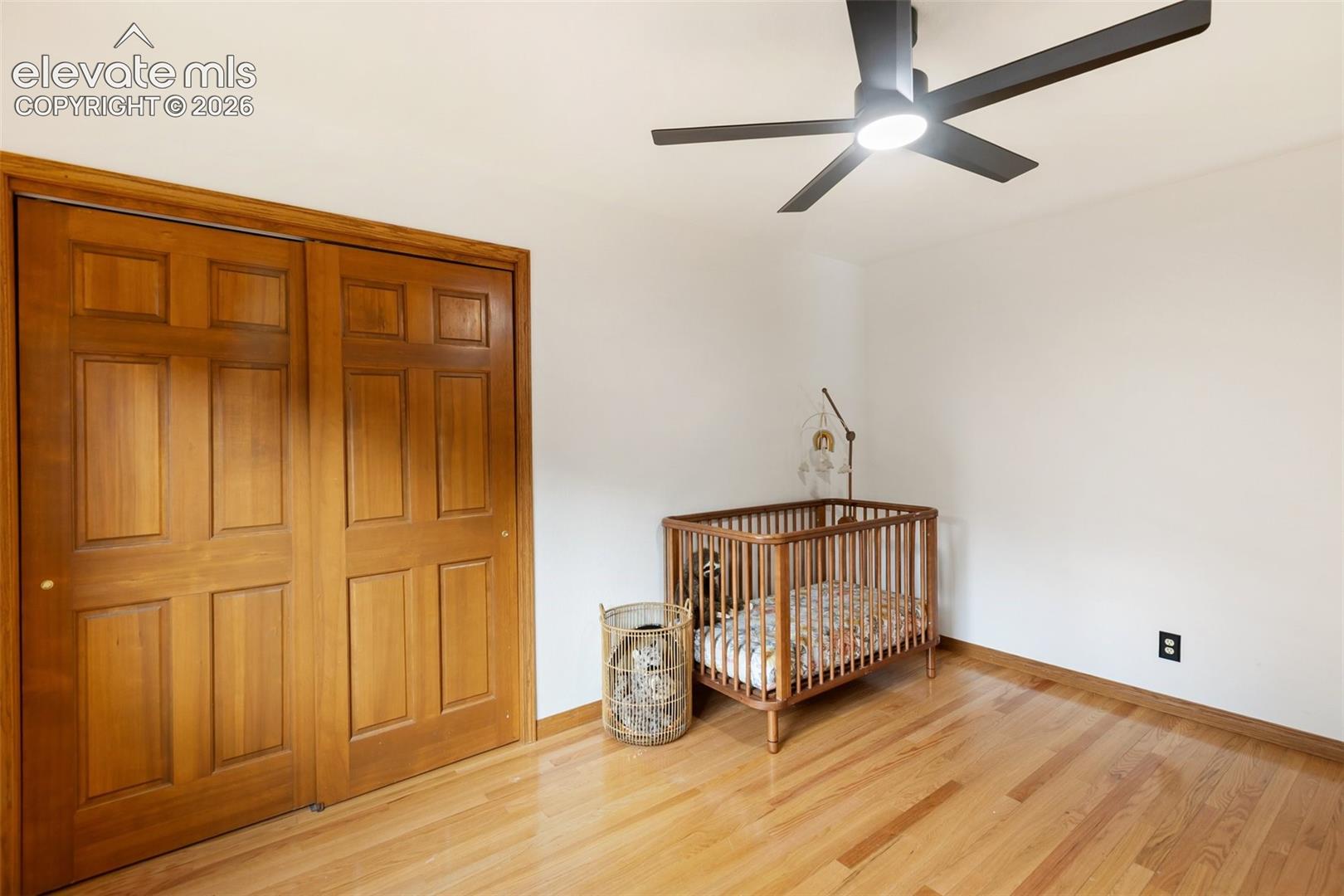 Wood-finish flooring, six-panel wood closet doors with matching trim, and a modern matte black ceiling fan with integrated lighting