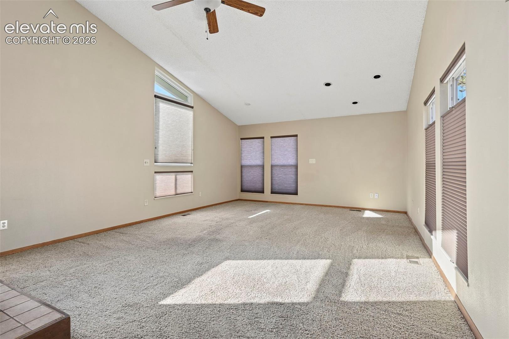 Vaulted ceilings, carpeting, multiple windows, recessed lighting, and a ceiling fan