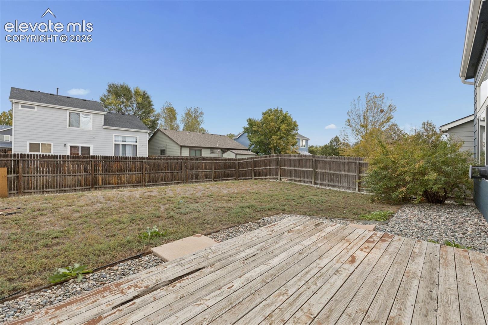 Rear yard featuring a wood deck, perimeter wood fencing, and gravel hardscaping