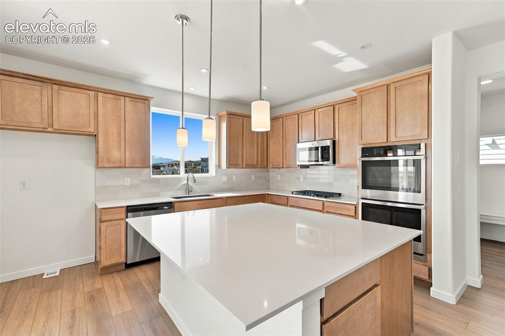 Kitchen featuring a central island with a light-toned countertop, wood-finish flooring, a stainless steel double oven, and pendant lighting