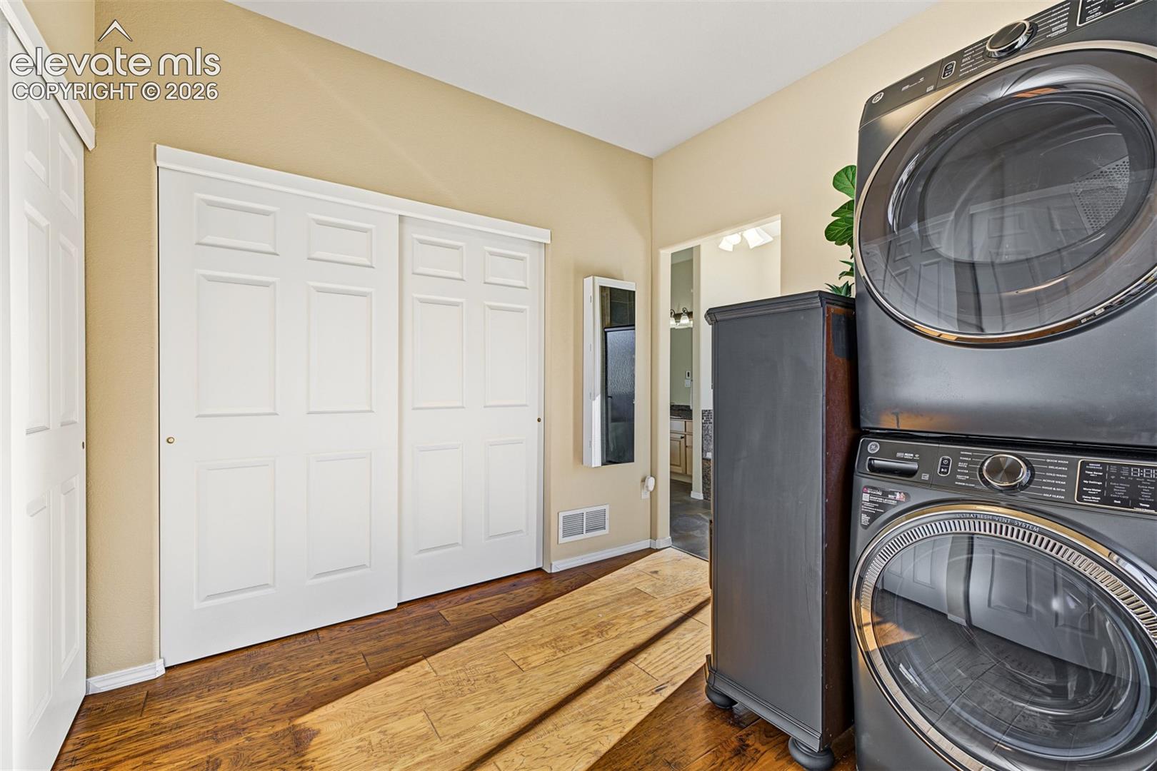 Primary bedroom walk-in closet featuring hardwood flooring, ample closet space, and the convenience of washer and dryer hookups with a stacked laundry configuration. Washer and dryer are excluded from the sale.