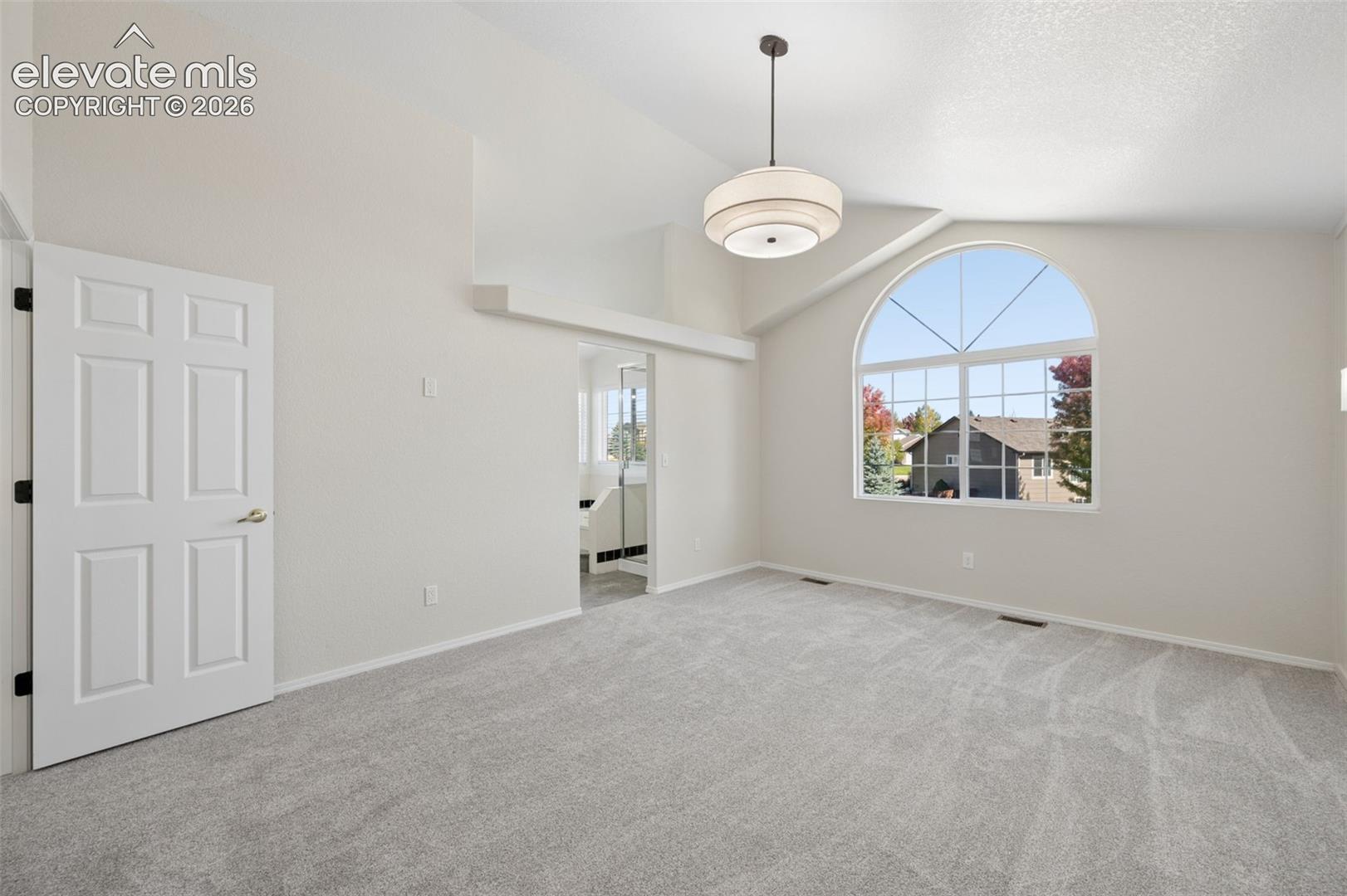 Vaulted ceilings featuring a drum pendant light fixture, arched window with a grid pattern, and carpeted flooring