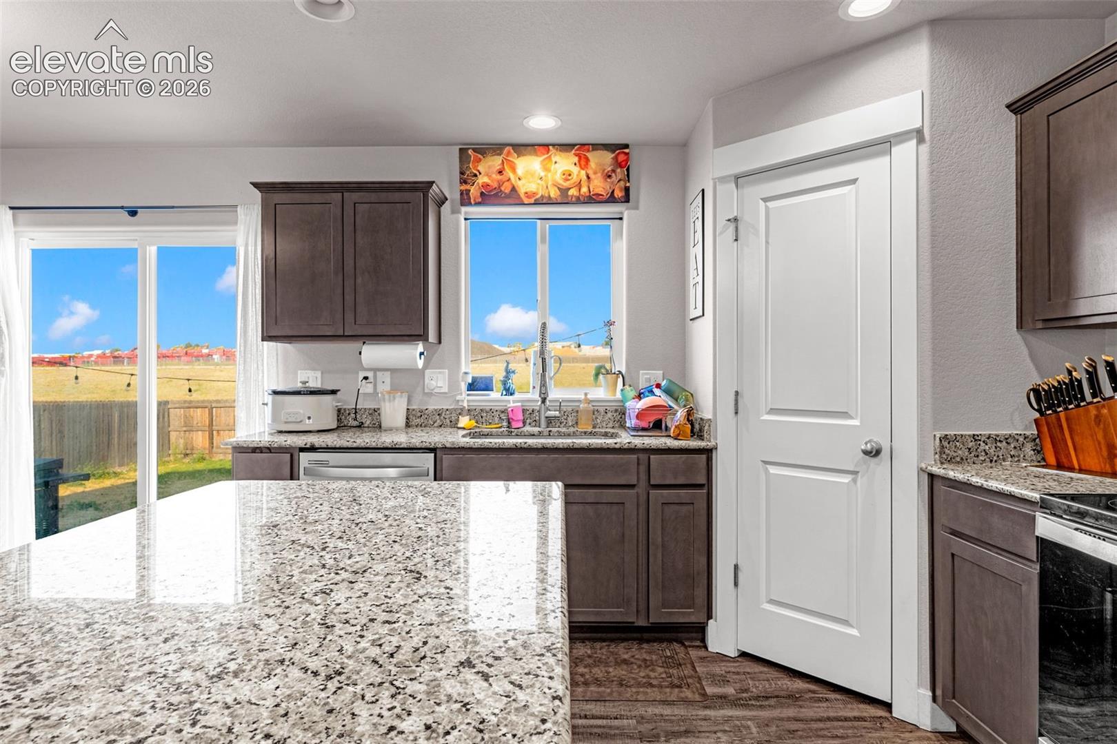 Kitchen featuring a stone-look countertop island, dark wood-finish cabinetry, stainless steel dishwasher, a window above the sink, and sliding glass doors to the exterior