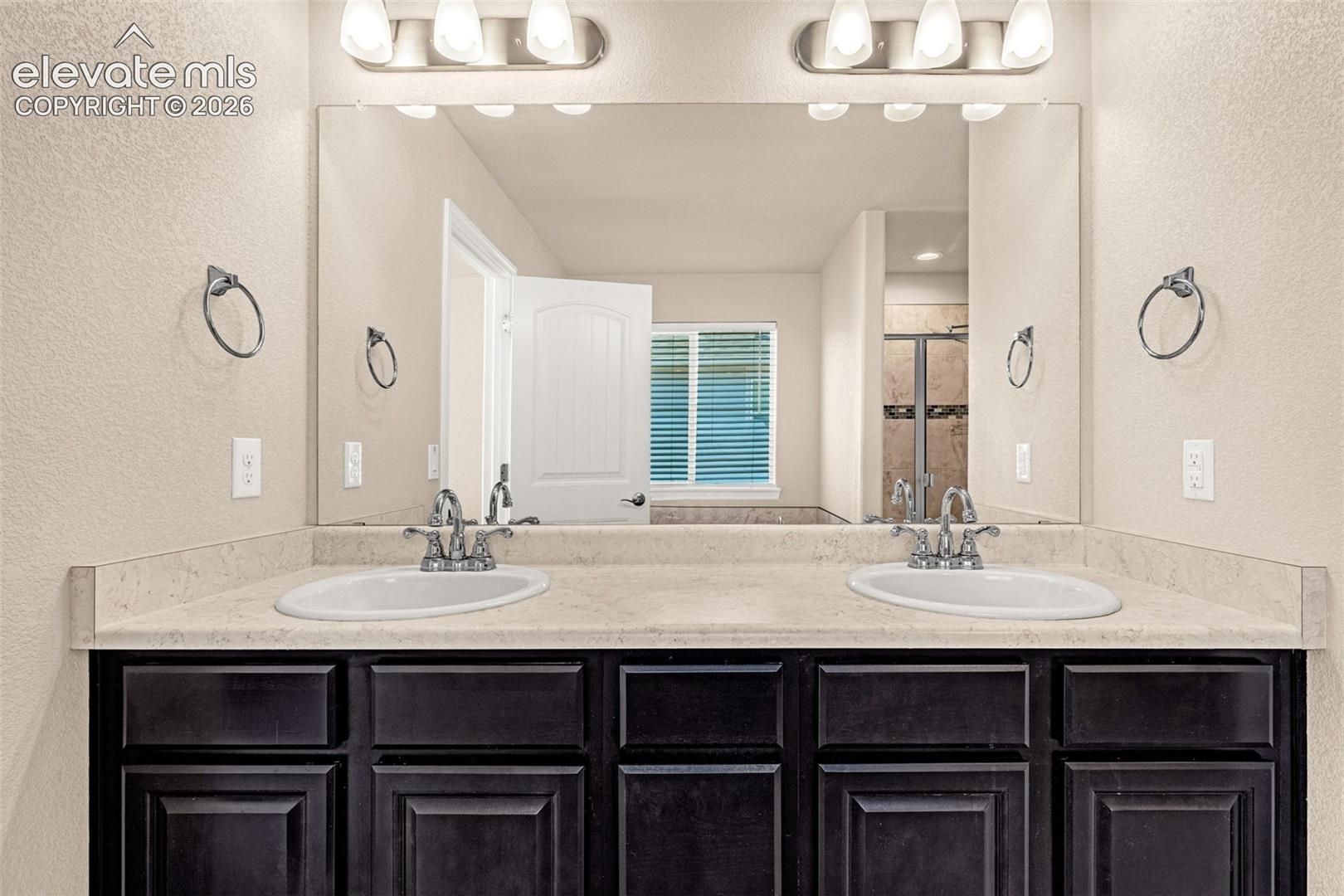 Dual vanity with integrated sinks, light-toned countertop, dark wood-finish cabinetry, and brushed nickel fixtures