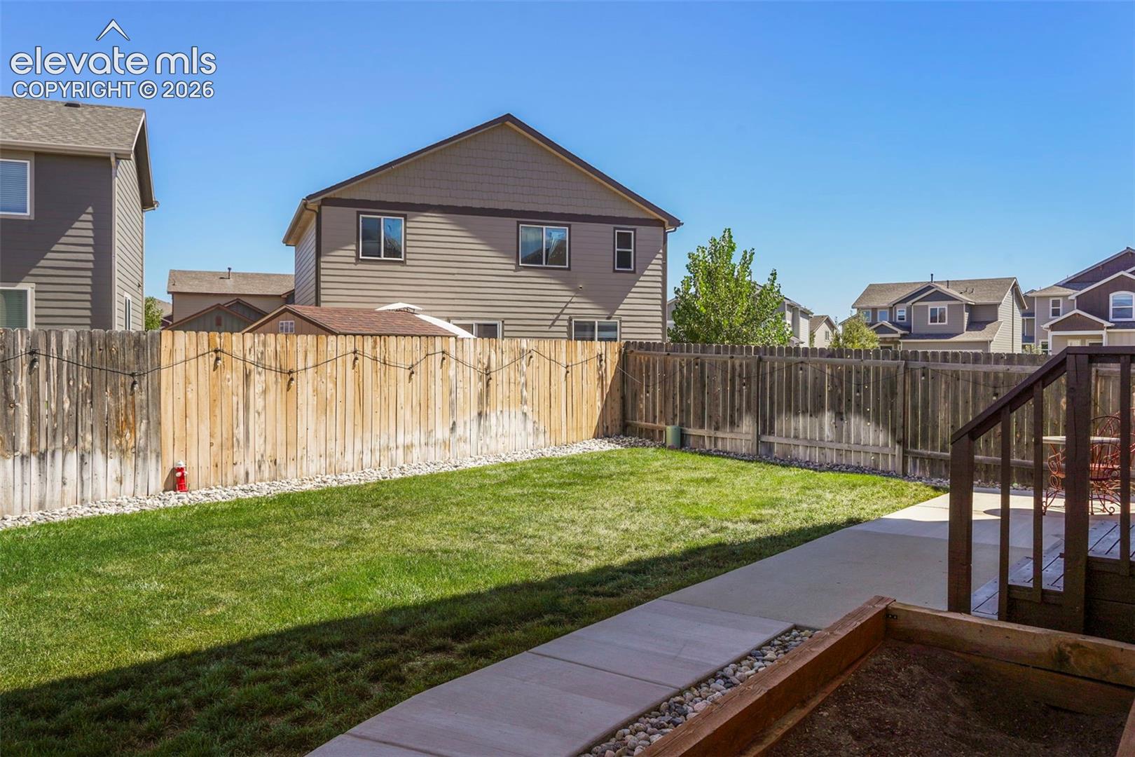 Expansive backyard featuring a manicured lawn, concrete patio, privacy fencing, and an elevated wood deck with railings