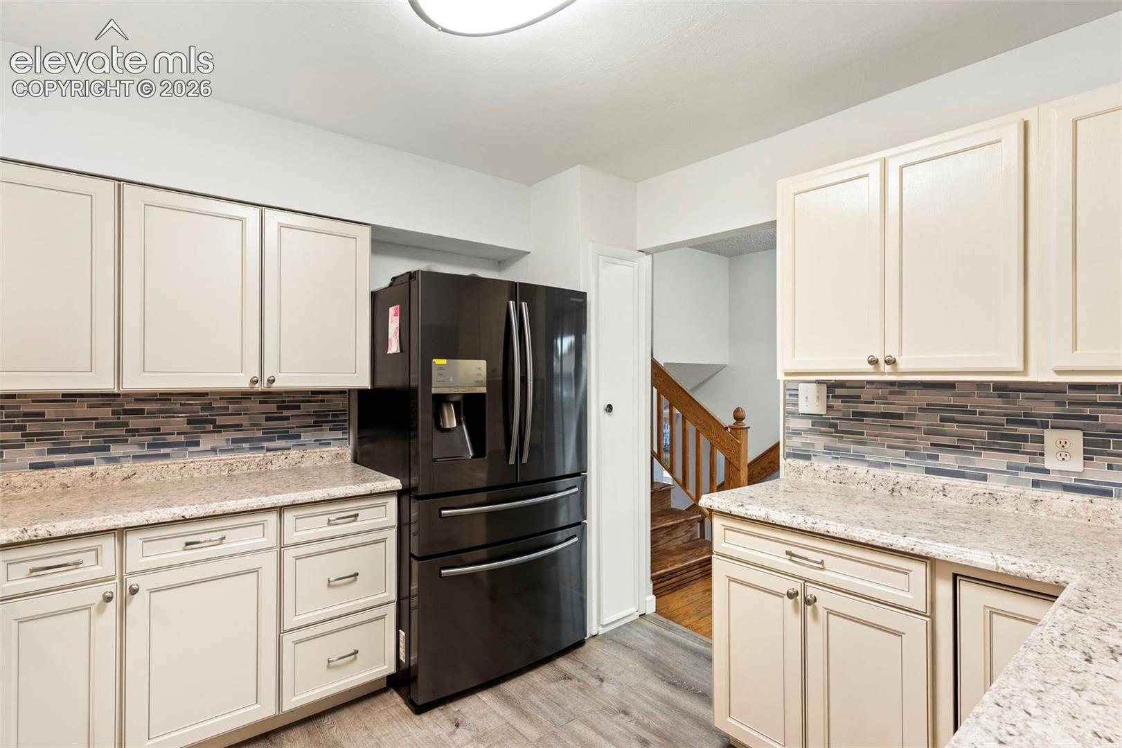 Cream-colored cabinetry with modern hardware, stone-finish countertops, tile backsplash, and wood-finish flooring