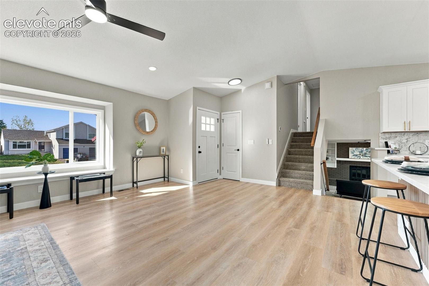 Vaulted ceilings, wood-finish flooring, large picture window, ceiling fan with integrated lighting, and carpeted staircase with handrail