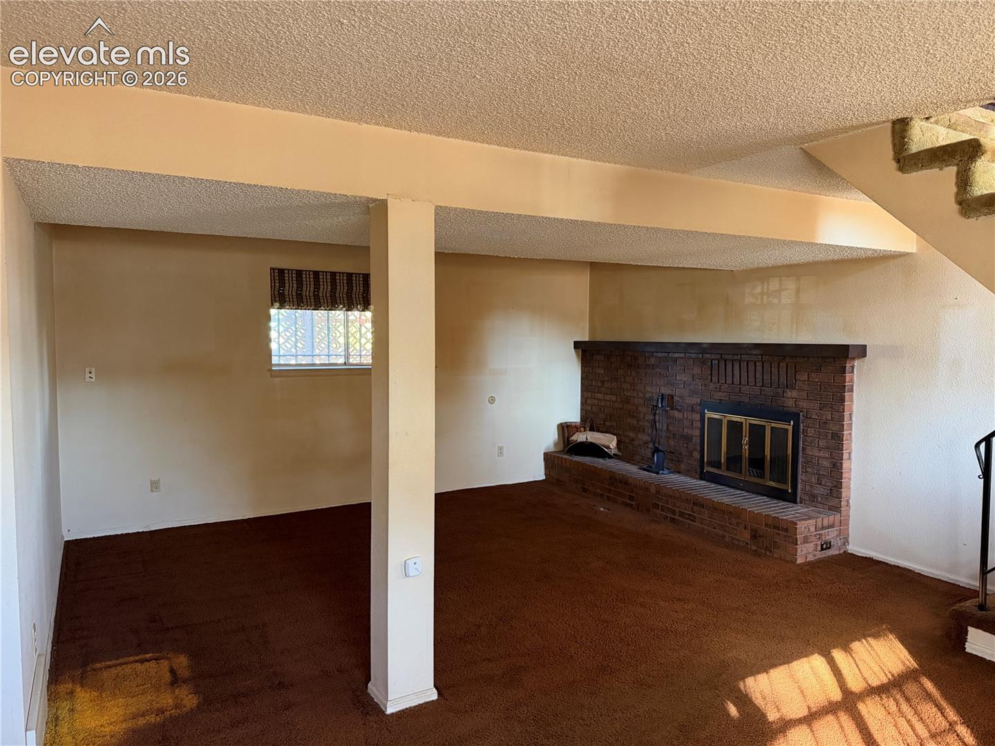 Red brick fireplace with a built-in hearth, textured ceiling, and structural pillar