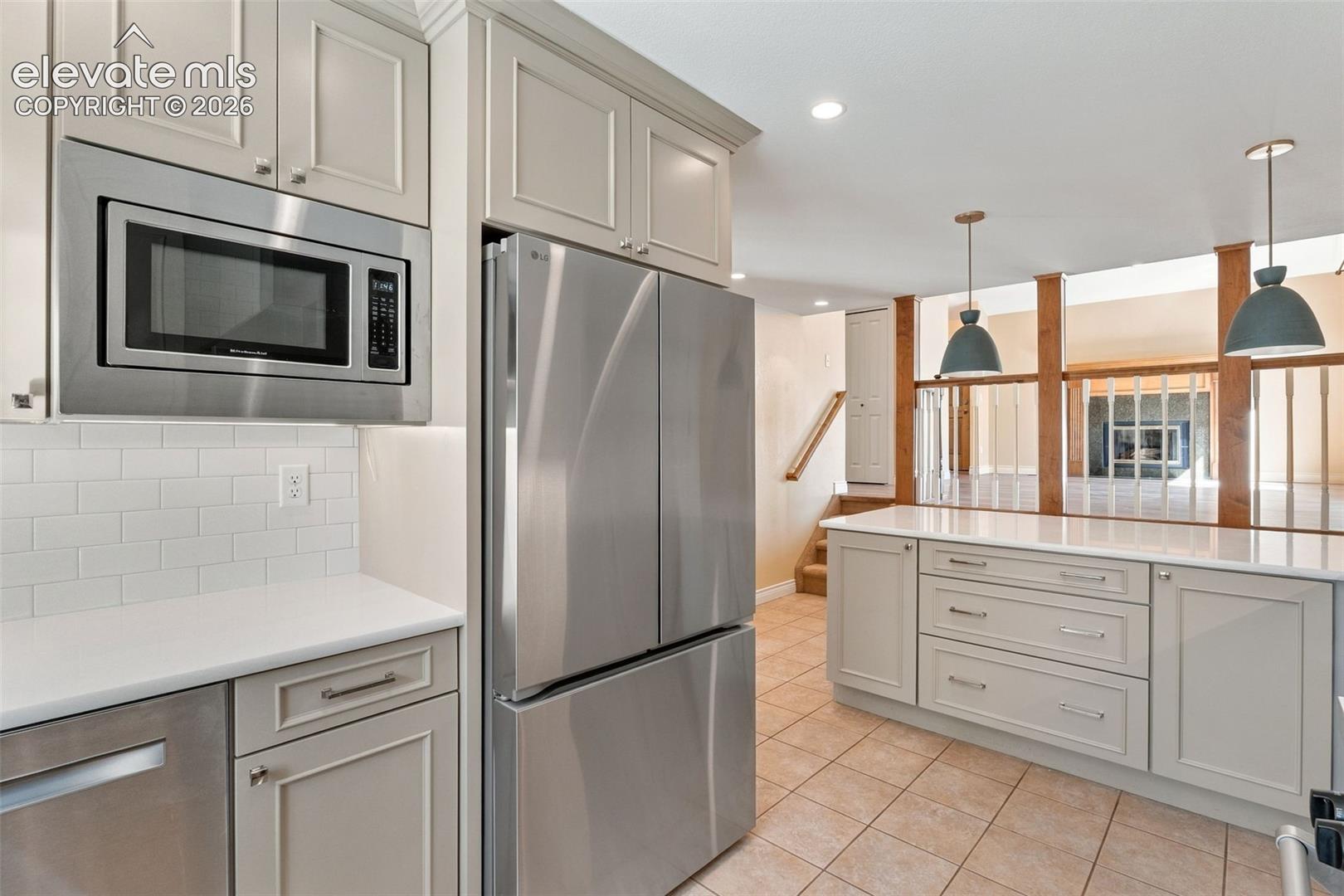 Kitchen featuring shaker-style cabinetry, stainless steel appliances, white subway tile backsplash, solid-surface countertops, and ceramic tile flooring
