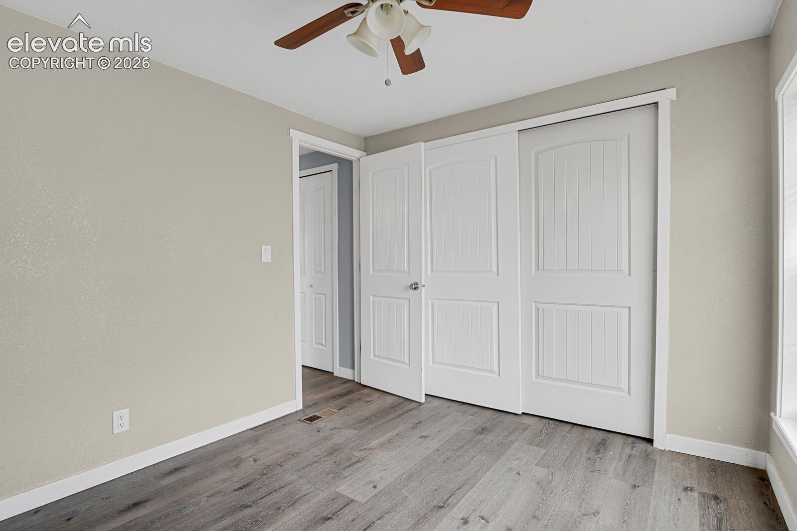 Wood-finish flooring, white trim, sliding closet doors, ceiling fan, and window with blinds