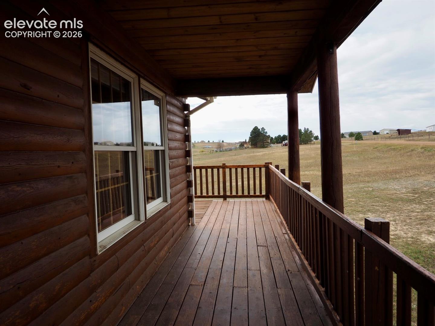 Covered log-sided porch featuring wood decking, vertical spindle railing, and exposed log exterior walls