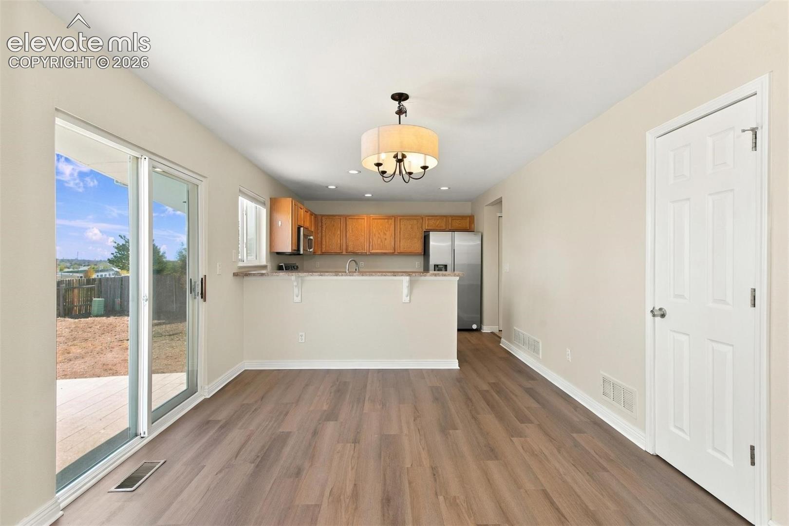 Open-concept interior featuring wood-finish flooring, a tiered breakfast bar, a drum-style pendant light fixture, and sliding glass doors