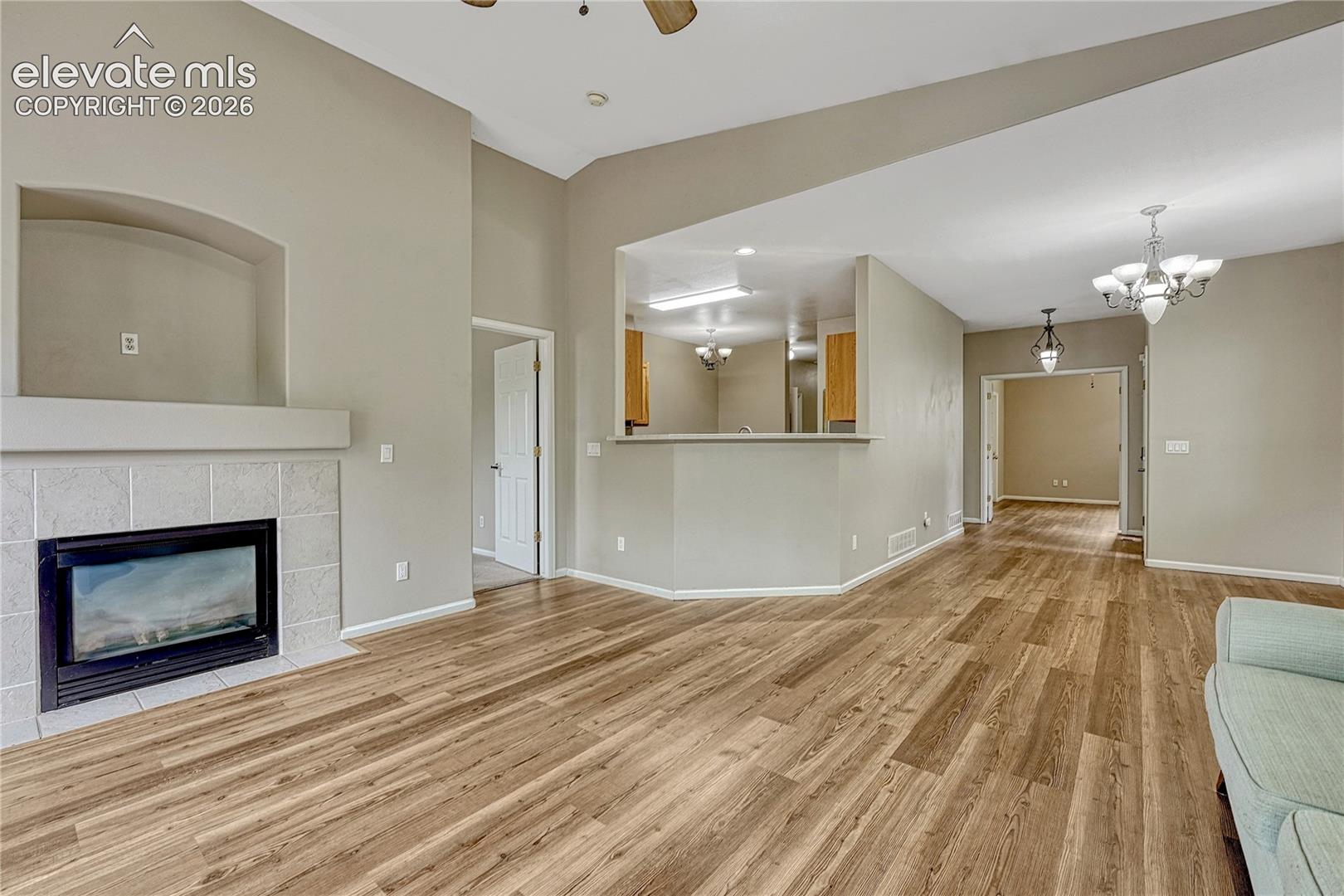 Vaulted ceilings with recessed lighting, wood-finish flooring, built-in fireplace with tile surround, arched wall niche, and kitchen pass-through with breakfast bar