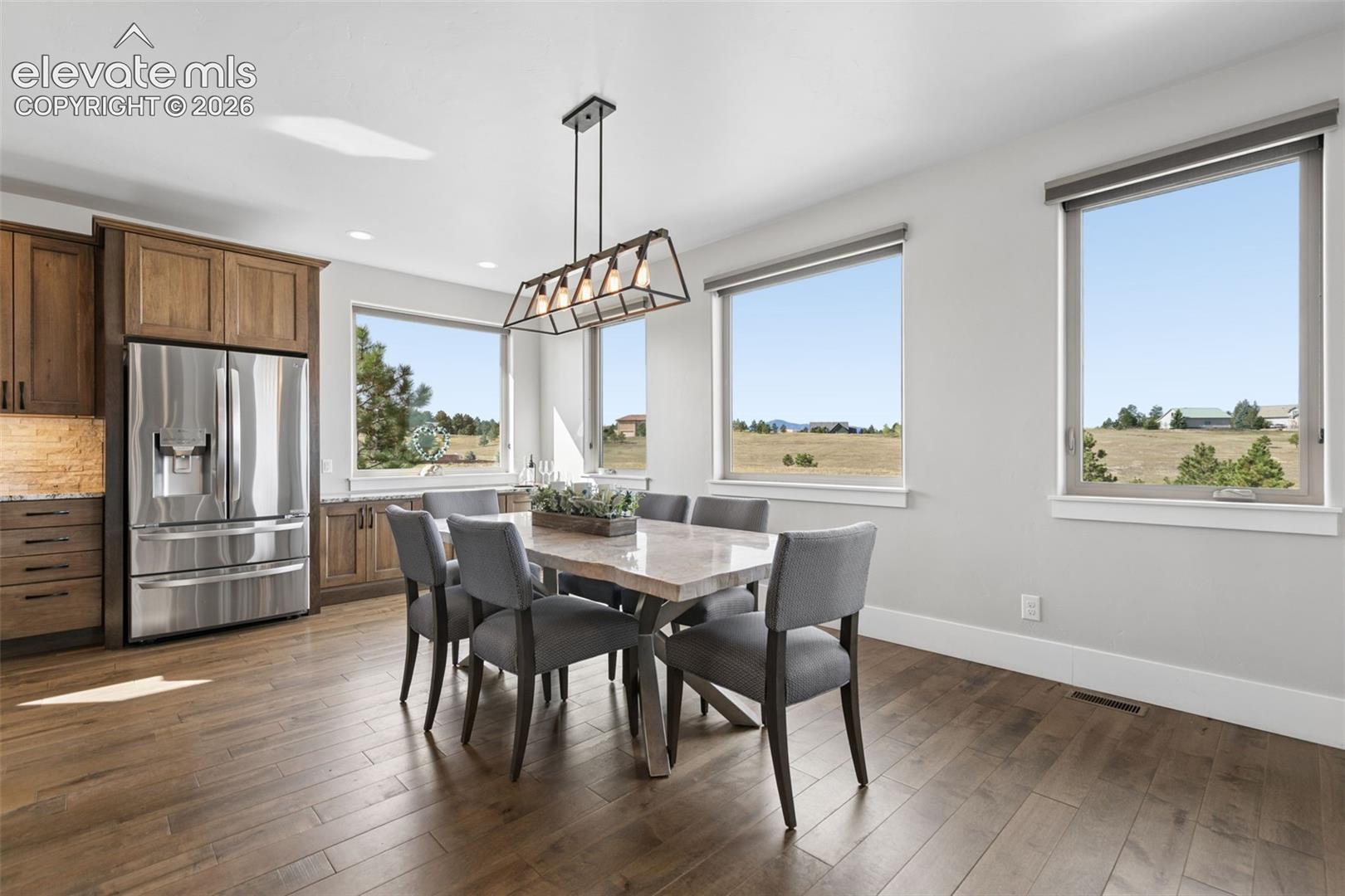 Hardwood flooring, wood cabinetry, stainless steel refrigerator, recessed lighting, and a linear pendant light fixture