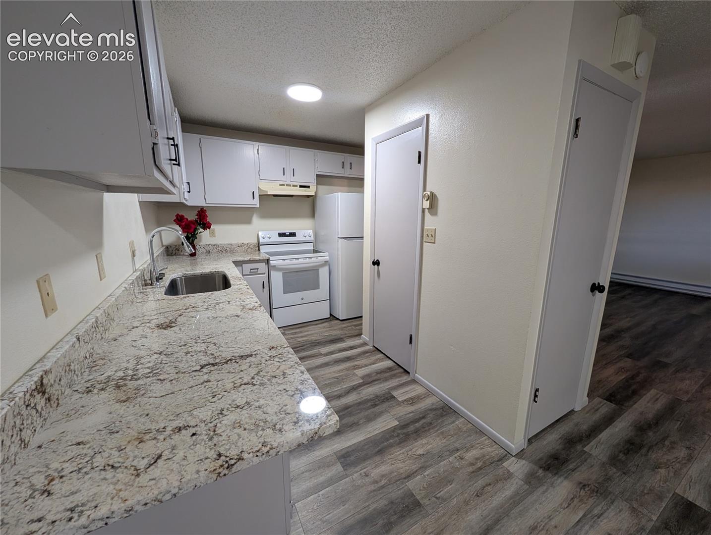 Kitchen featuring light-colored granite countertops, white cabinetry with black hardware, and a stainless steel sink with a high-arc faucet