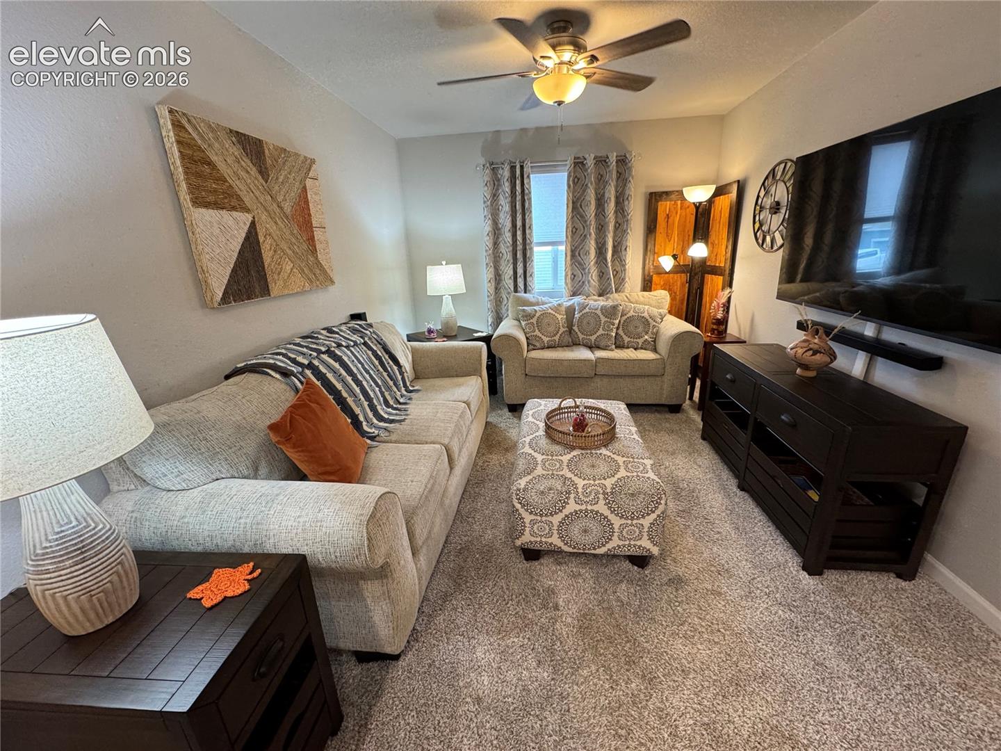 Neutral-toned carpeting, ceiling fan with integrated lighting, and single window with double-panel drapery
