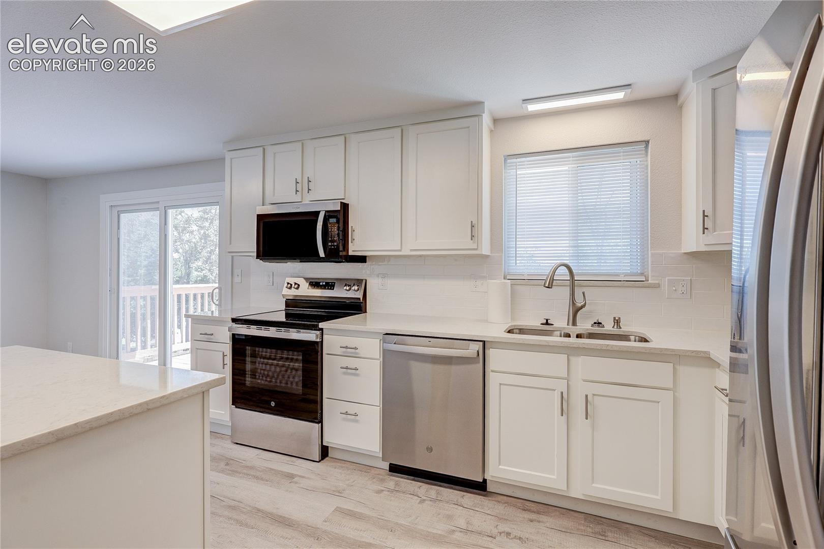 Kitchen featuring white cabinetry, quartz countertops, stainless steel appliances, a double-basin undermount sink, and wood-finish flooring