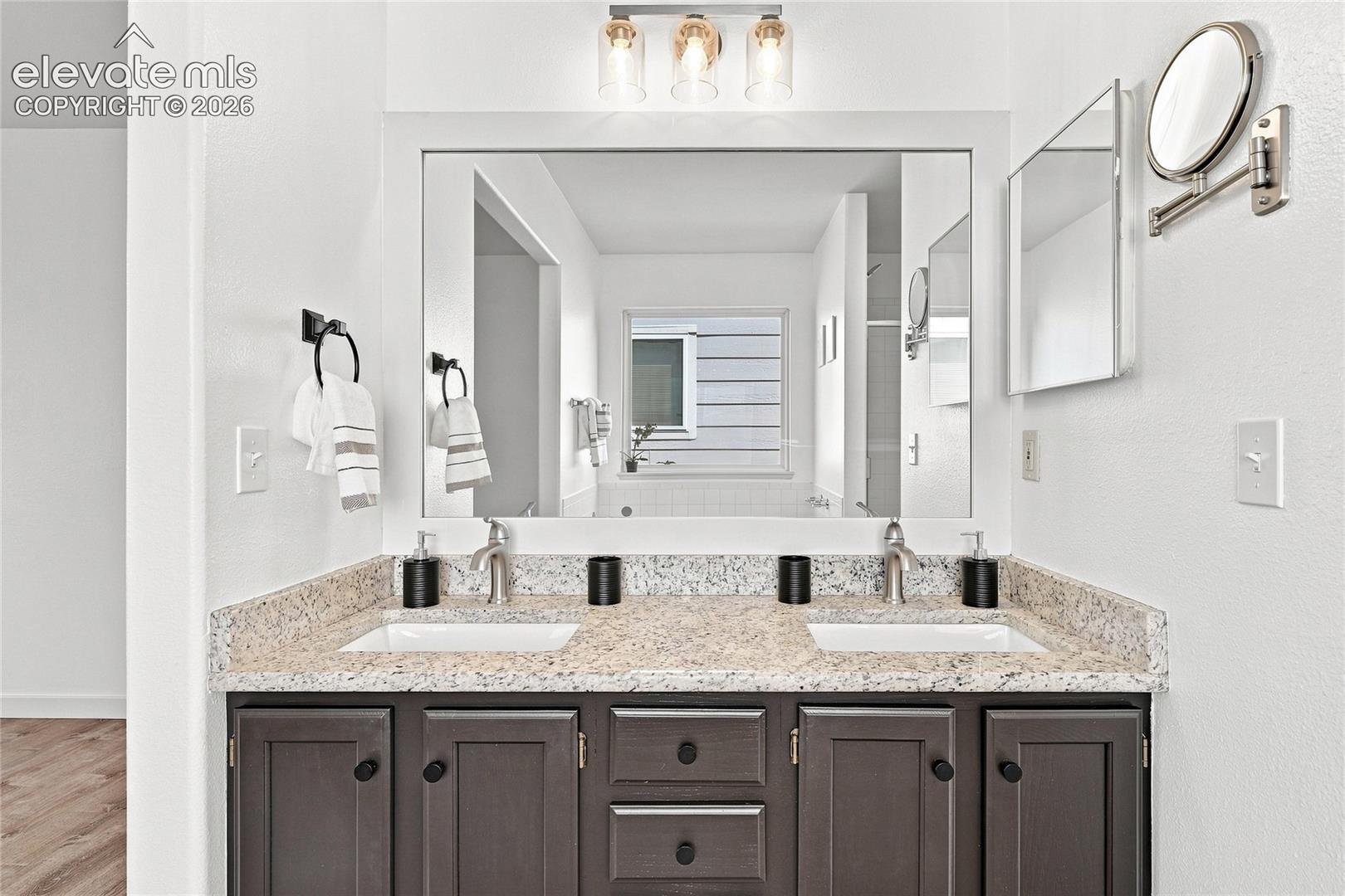 Dual basin vanity with a speckled countertop, dark wood-finish cabinetry, and brushed nickel hardware