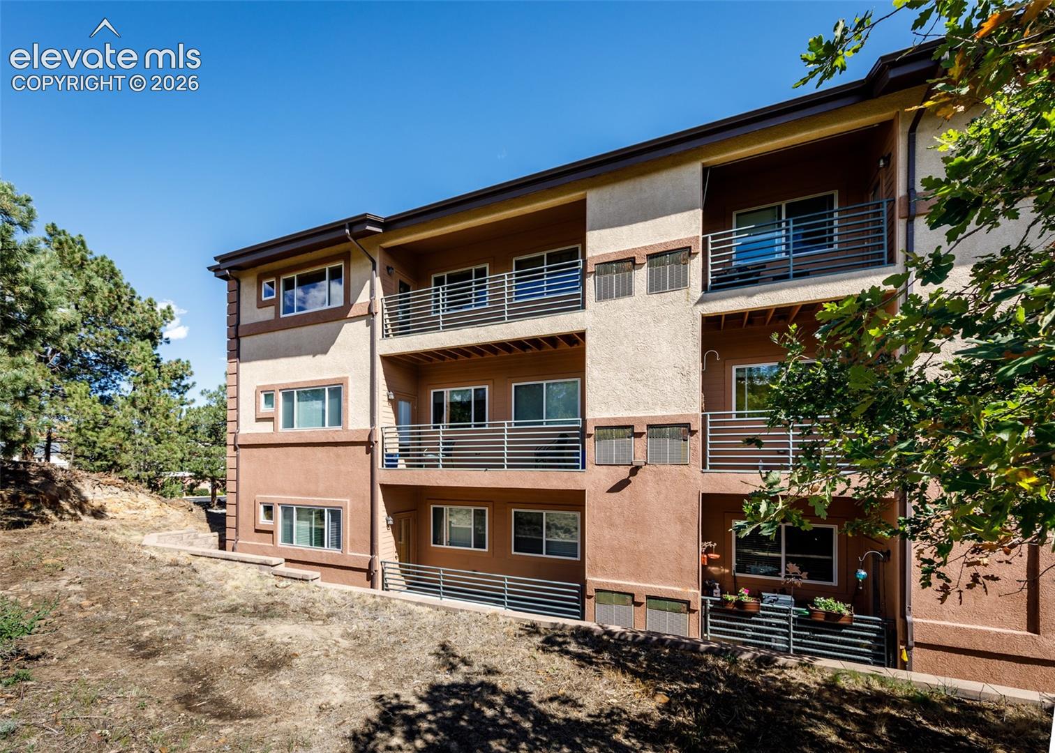 Multi-story exterior featuring a textured stucco facade, metal balcony railings, and dual-pane windows