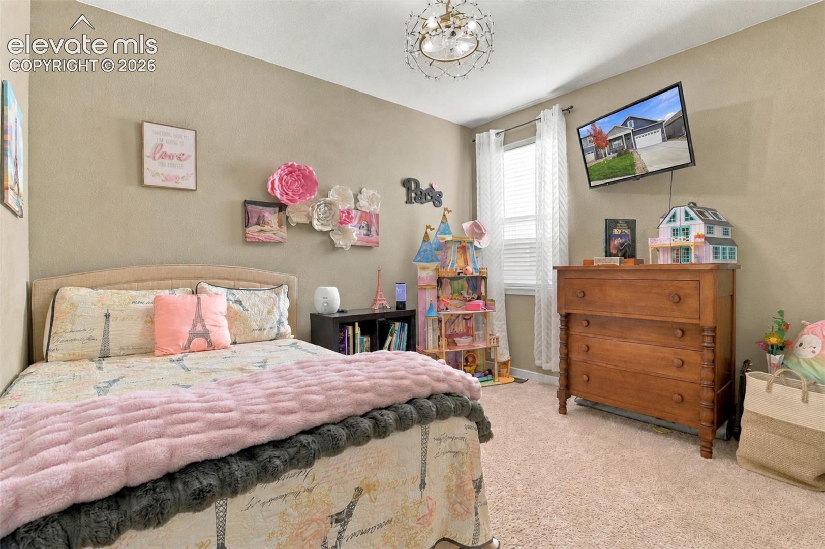 Neutral-toned room featuring wall-to-wall carpeting, a multi-tiered crystal-style chandelier, and a window with floor-length white drapery