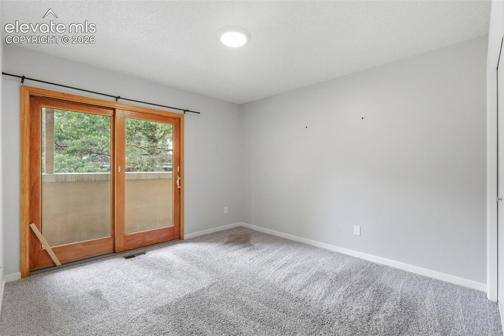 Bedroom featuring light wood-frame sliding glass doors, a balcony with a stucco-finish railing, and a textured ceiling with a flush-mount light fixture