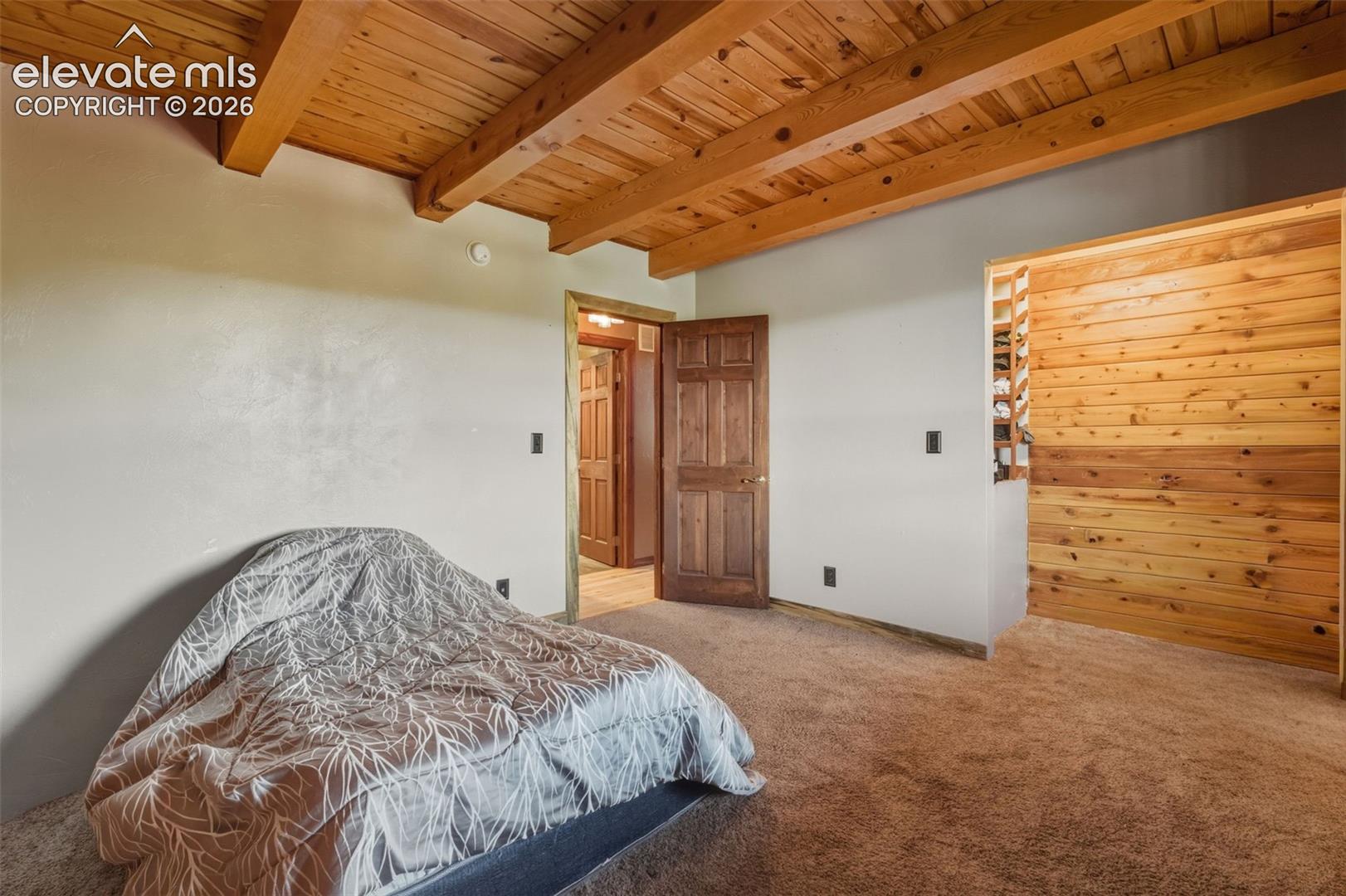 Exposed wood beam ceiling, wood plank wall accent, wood-finish door, and neutral-toned carpeting