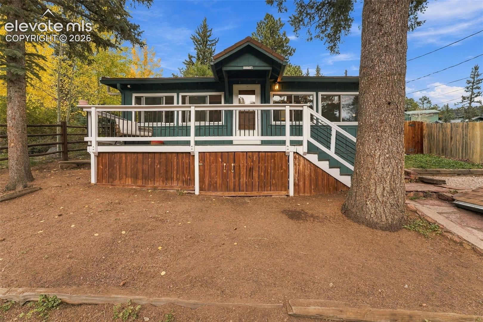 Exterior featuring a green-sided cabin with a white wooden deck, horizontal railings, and integrated under-deck storage cabinets