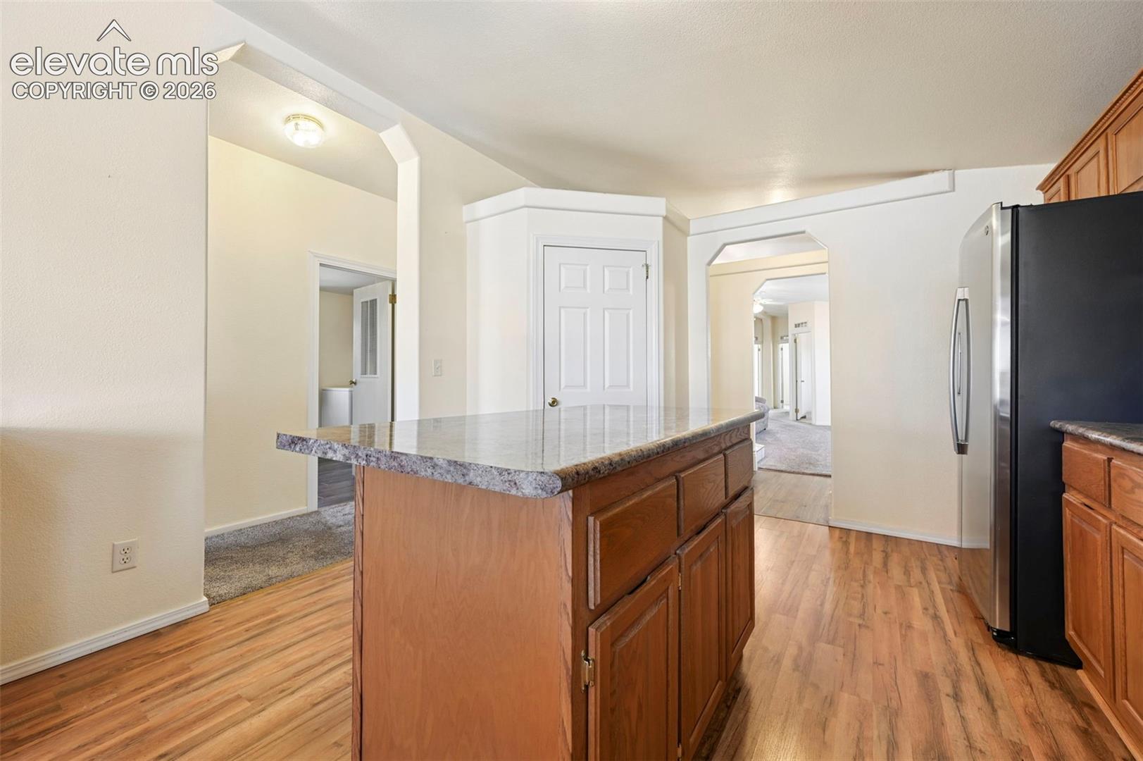 Kitchen featuring a center island with a stone-finish countertop, wood-finish cabinetry, wood-finish flooring, and a stainless steel refrigerator
