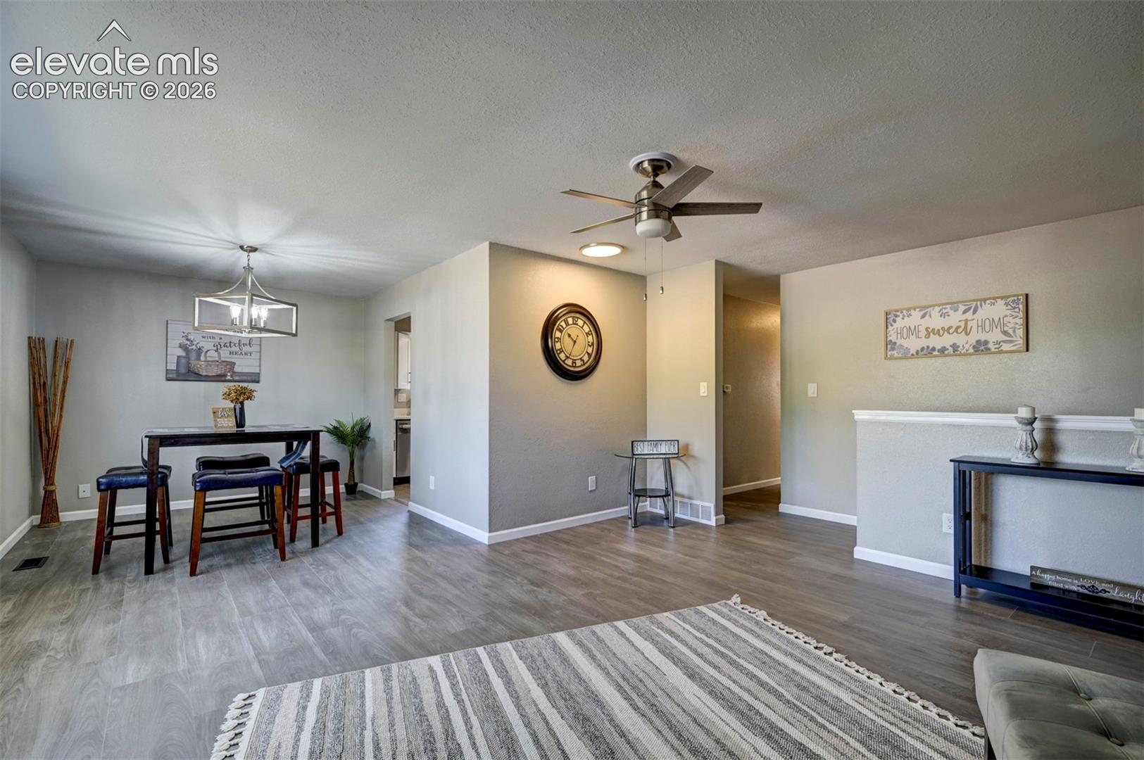 Neutral-toned living space featuring wood-finish flooring, a ceiling fan with integrated lighting, and a modern geometric pendant light fixture