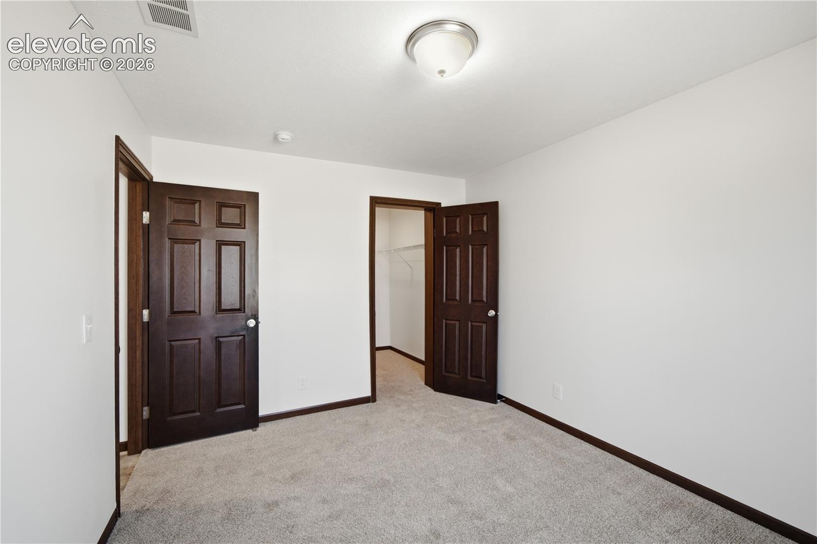 Neutral white wall finish, plush grey carpeting, dark wood-finish paneled doors, and a flush mount ceiling light fixture