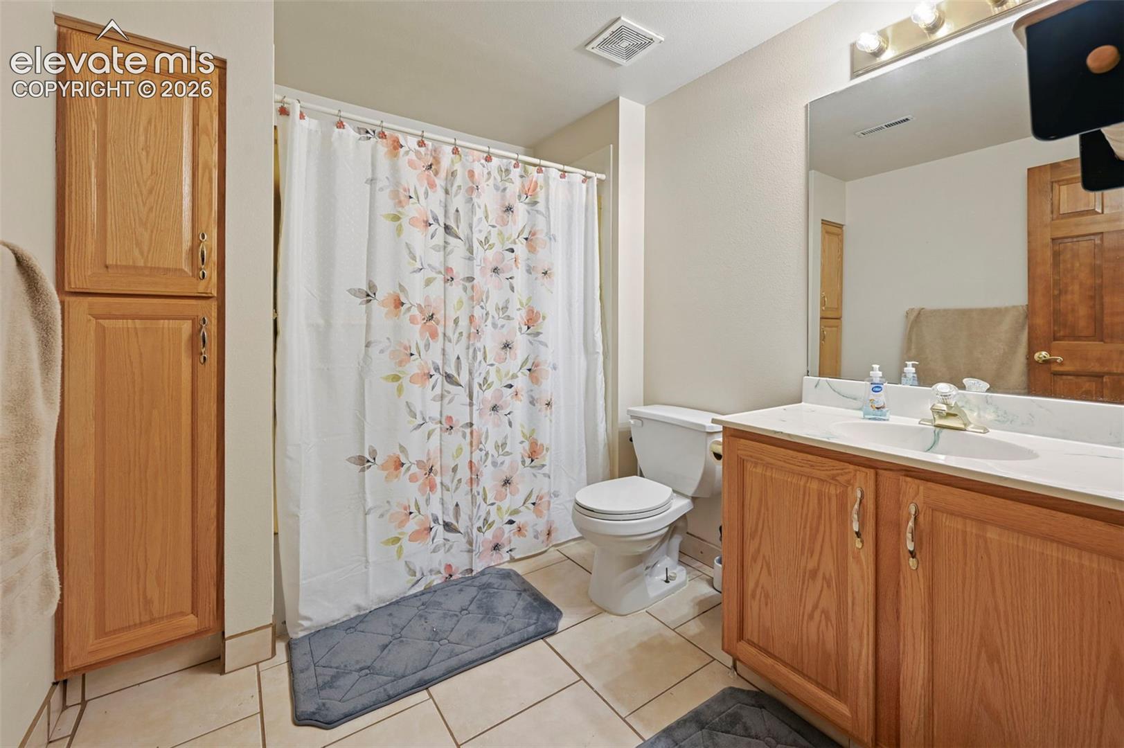 Basement bathroom featuring a vanity with wood cabinetry, a white countertop, an integrated sink, a large mirror, and tiled flooring