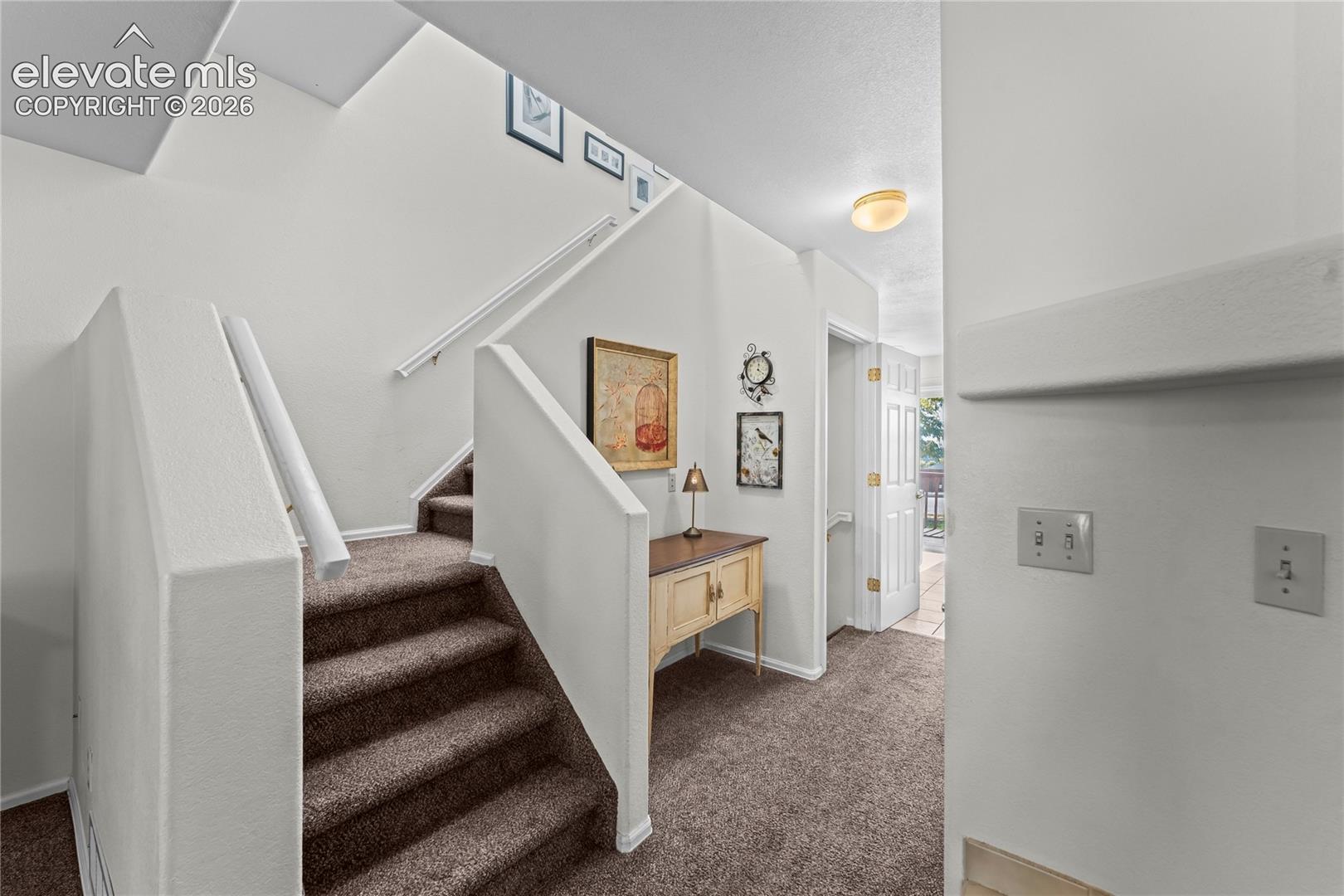 Carpeted staircase with white handrails and wall-mounted light fixture