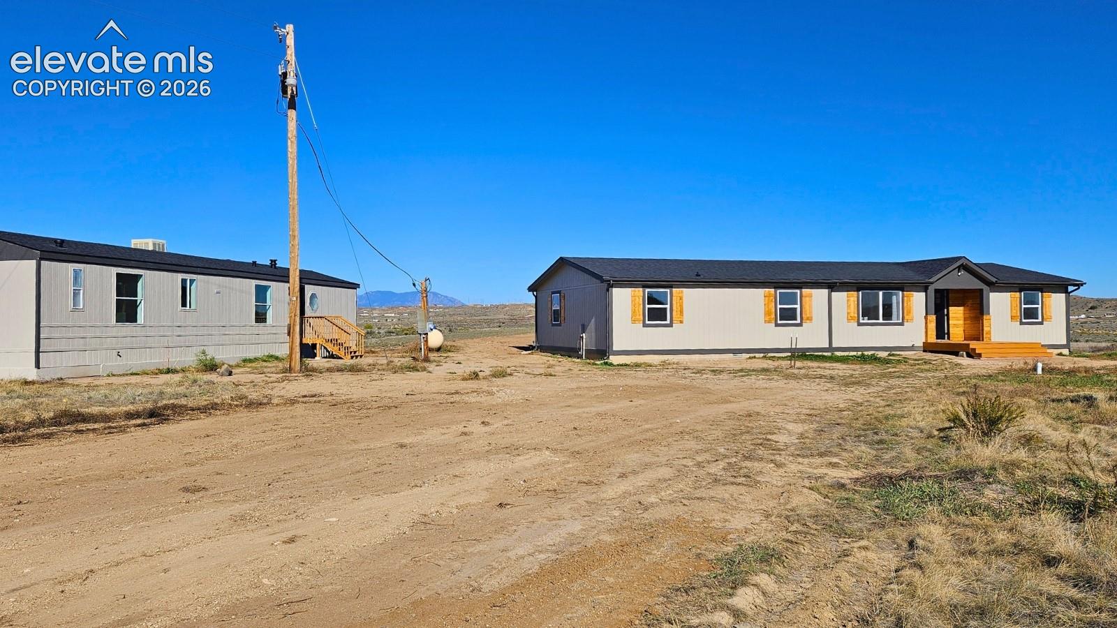 Exterior profile featuring dual structures, neutral-toned siding, dark metal roofing, wood-finished window shutters, and wood-framed entry steps