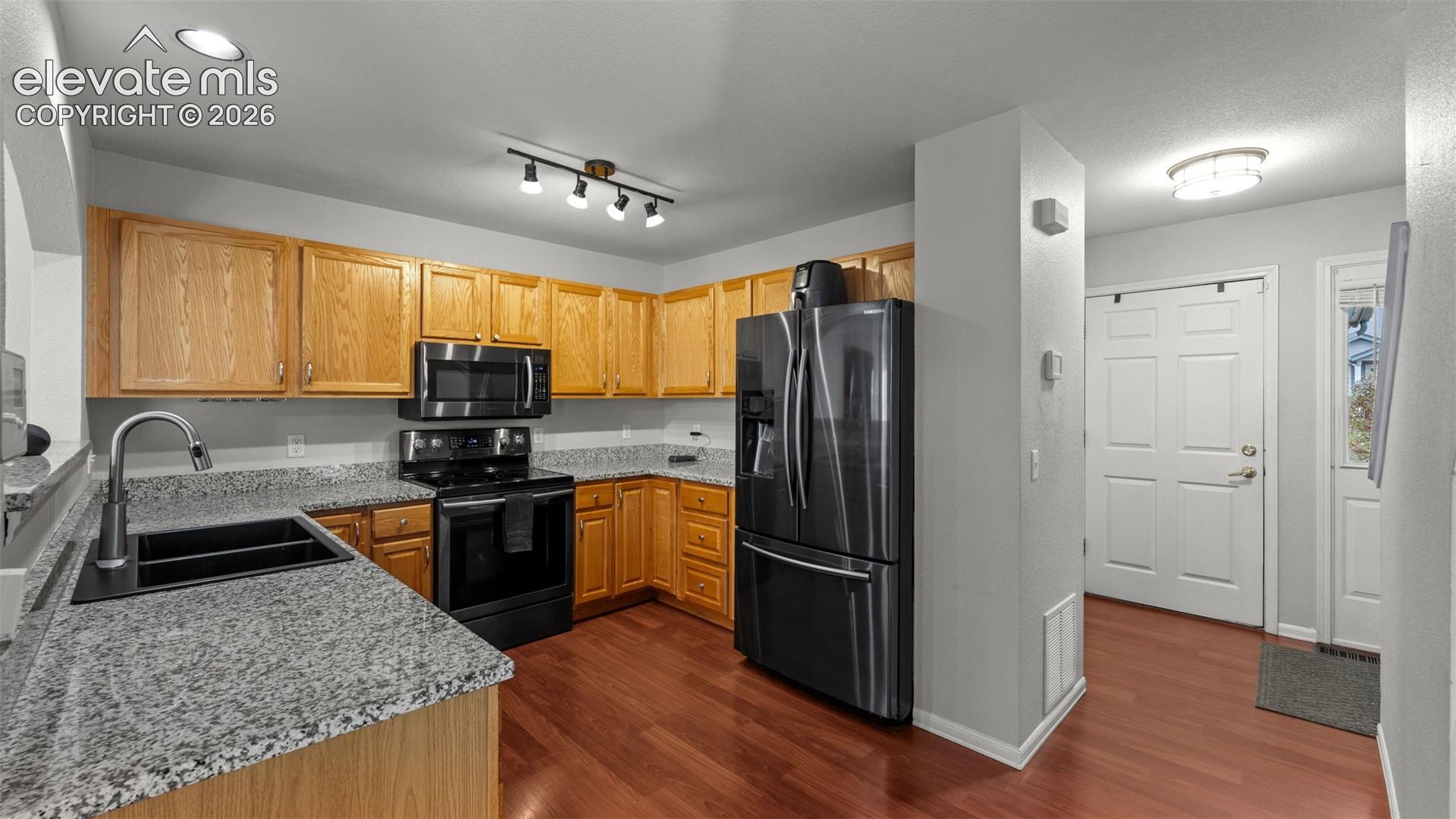 Kitchen featuring wood cabinetry, stone-finish countertops, black appliances, wood-finish flooring, and recessed ceiling lighting