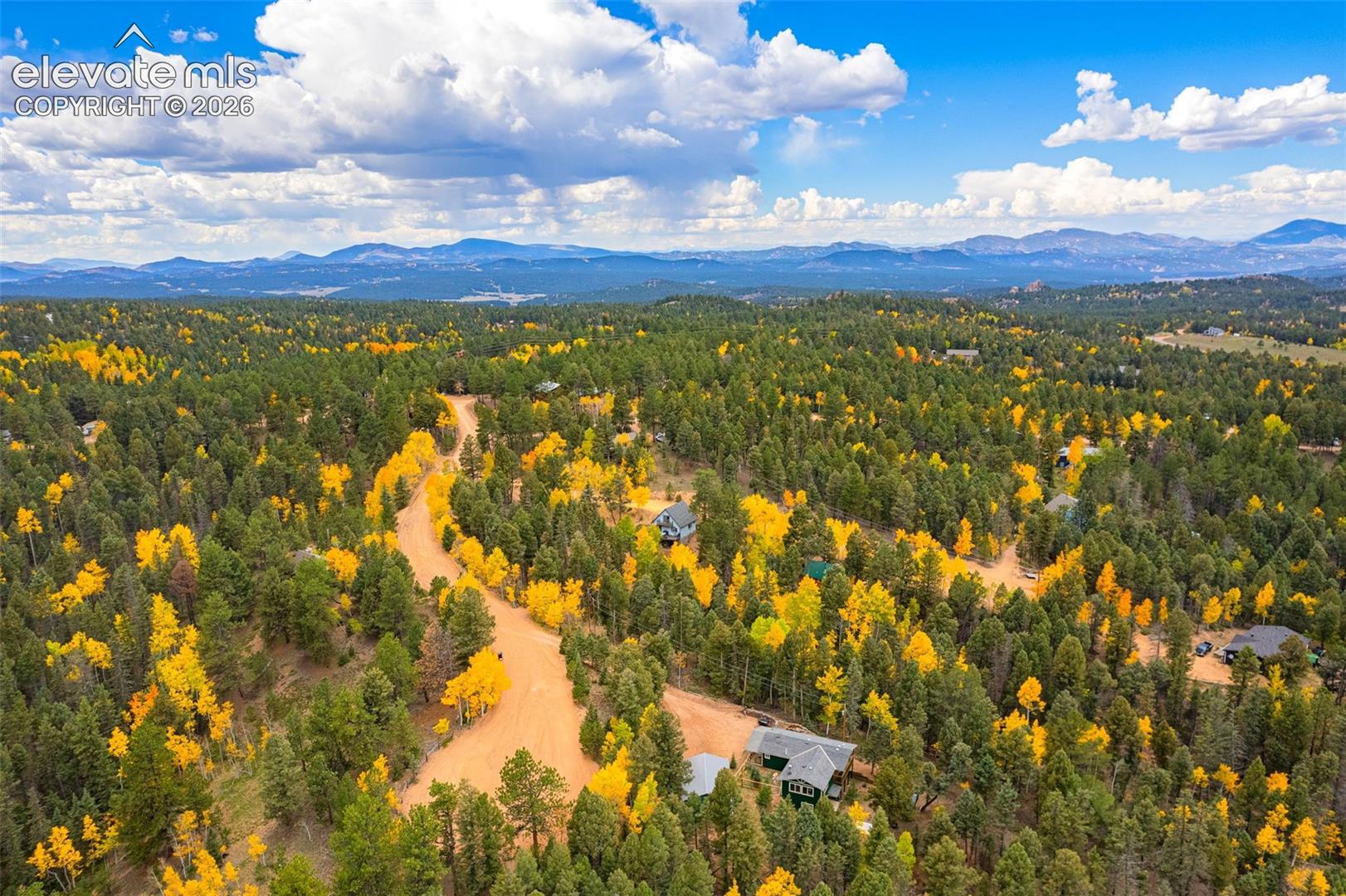 Aerial view featuring expansive mountain terrain, dense evergreen forest, and mature deciduous trees