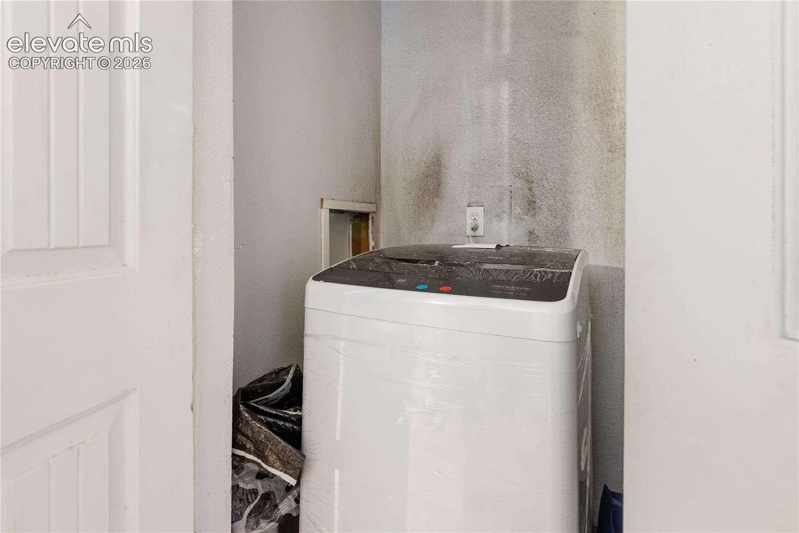 Enclosed laundry alcove with dedicated electrical outlet and wall-mounted plumbing access panel