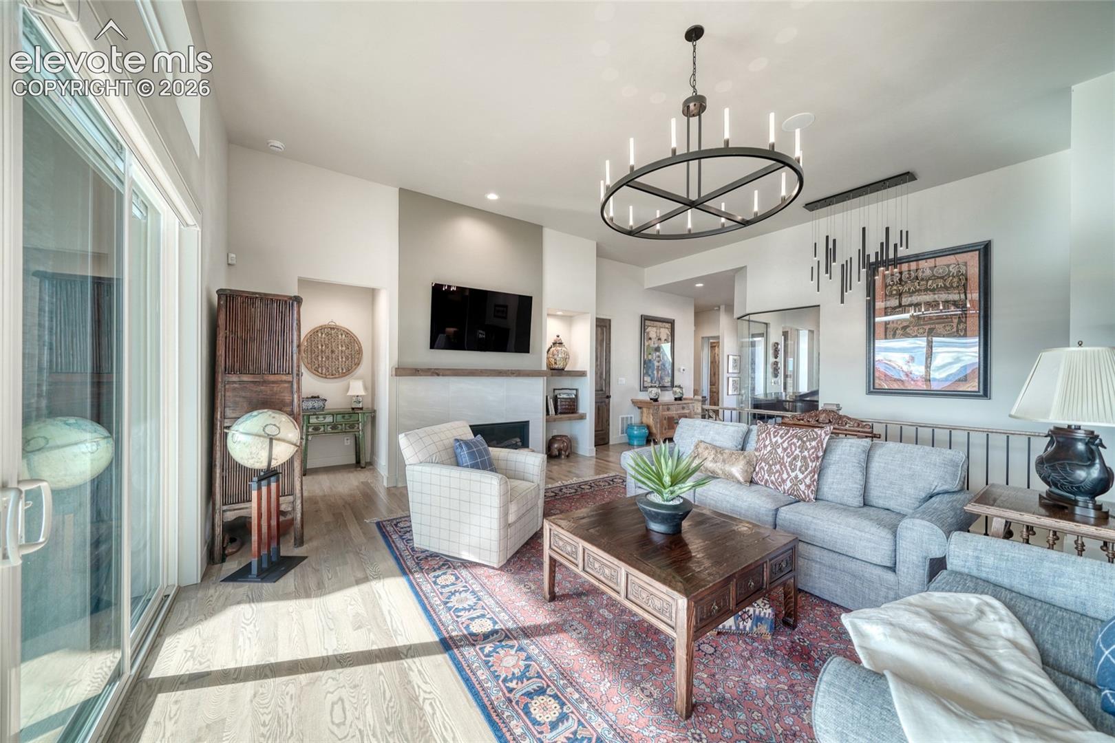 Living area featuring wood-finish flooring, a fireplace with a mantel, built-in shelving, a large circular candle-style chandelier, and floor-to-ceiling sliding glass doors