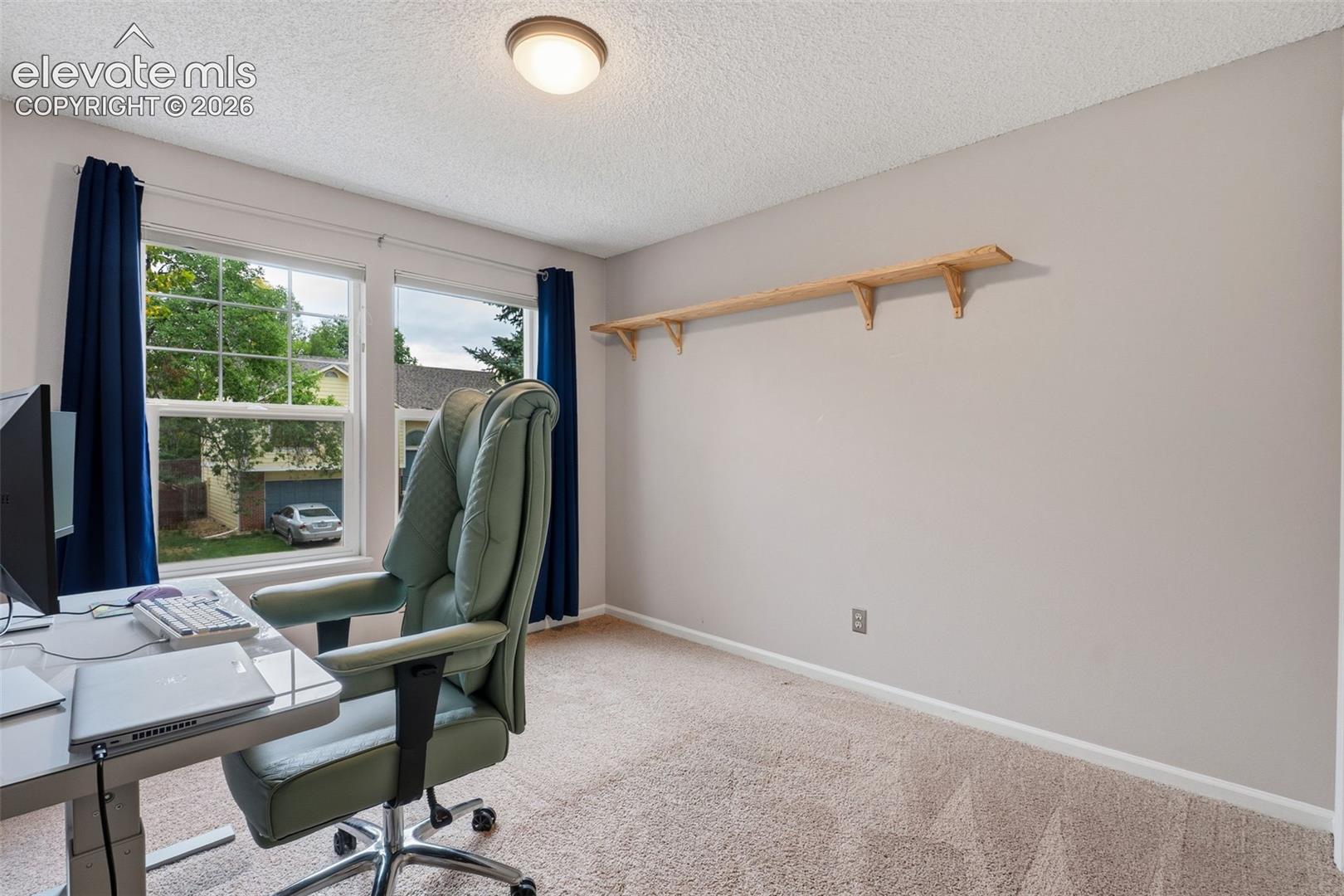 Twin windows with white frames, wall-mounted wooden shelving, and neutral tone carpeting
