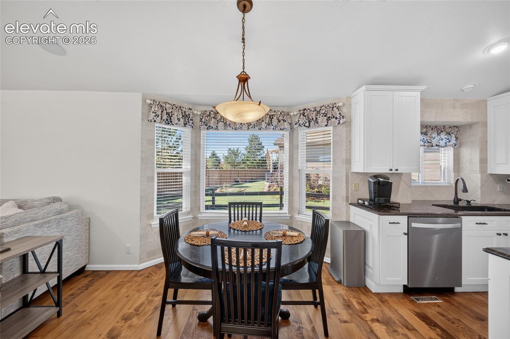 Kitchen featuring a bay window, white cabinetry, dark countertops, wood-finish flooring, and a pendant light fixture