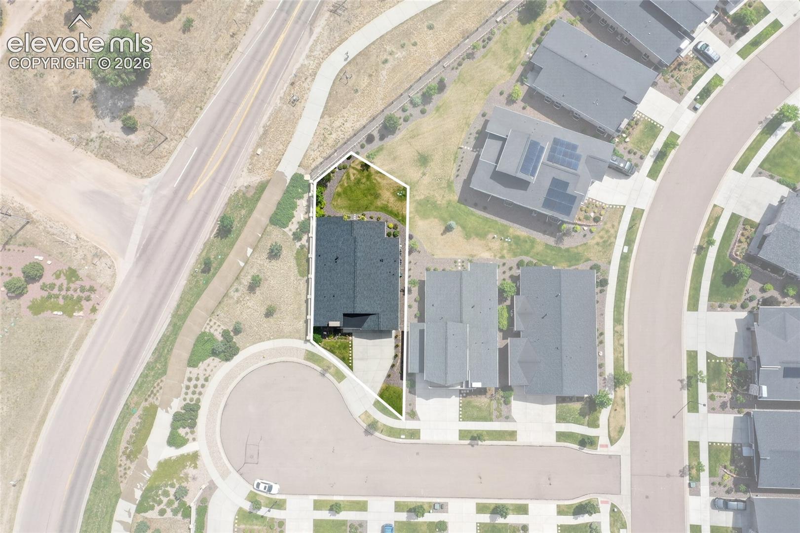 Aerial view showcasing a residential property with a dark shingle roof and a paved driveway