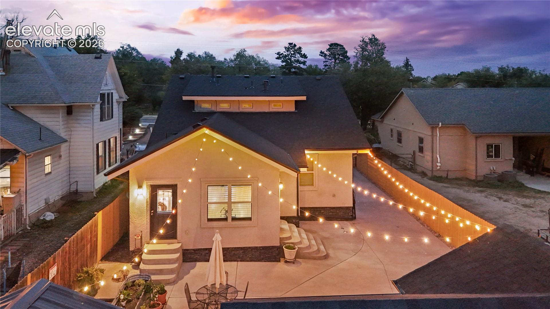 Rear exterior featuring a concrete patio, string lighting, and a dark asphalt shingle roof