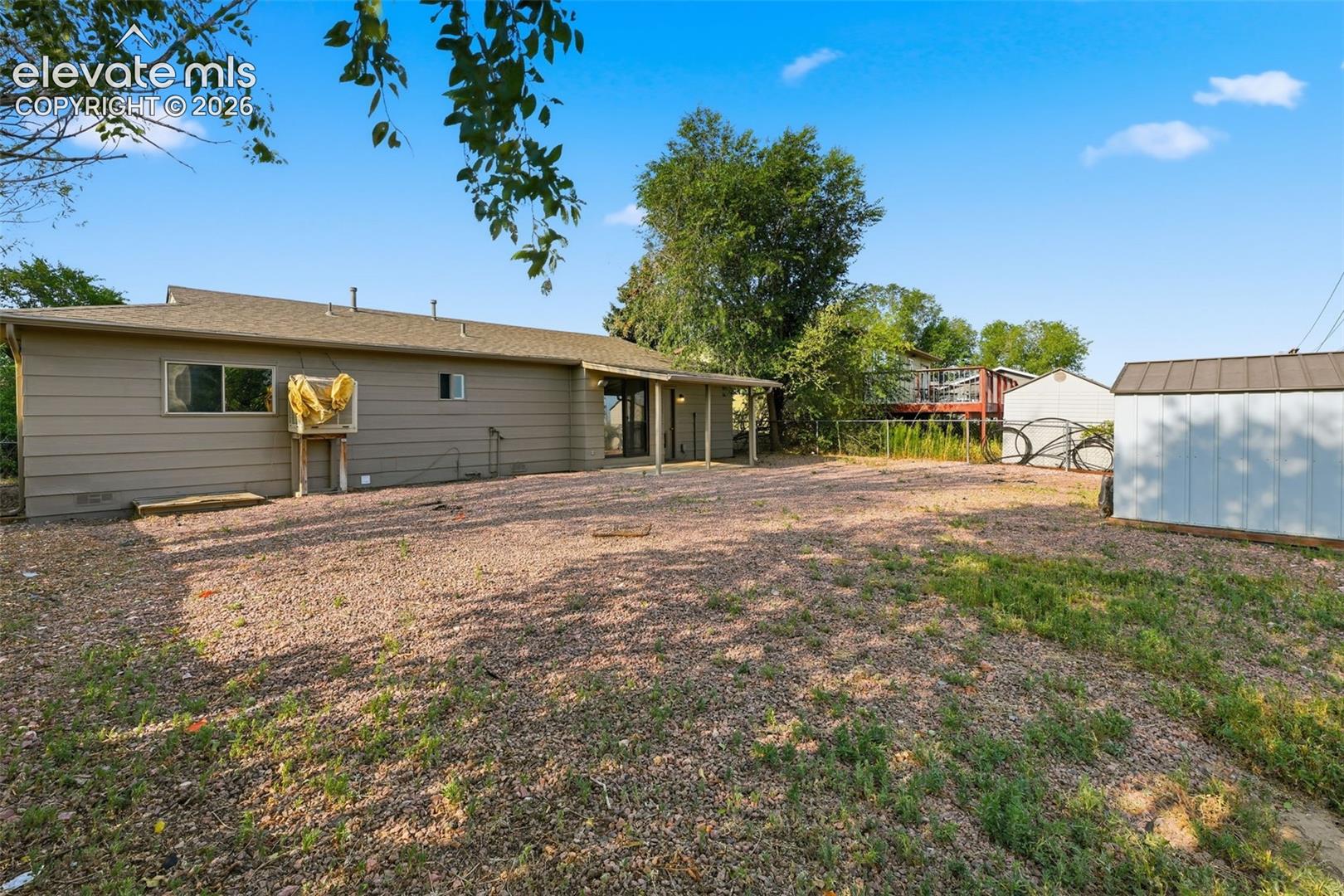 Expansive rear yard featuring a gravel patio, mature trees, and a detached storage shed