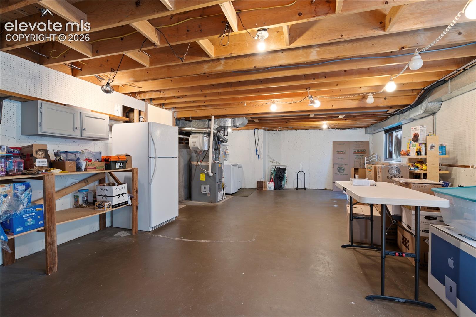 Expansive unfinished basement featuring an exposed wood joist ceiling, concrete flooring, and a window providing natural light