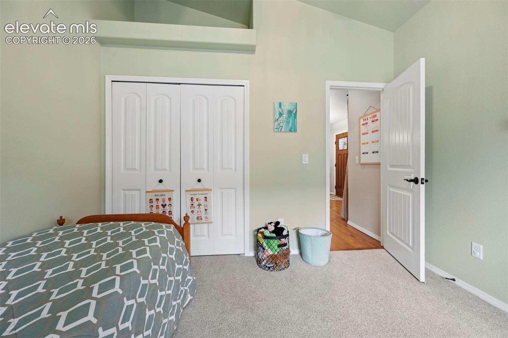 Room featuring vaulted ceilings, neutral carpeting, and built-in bi-fold closet doors with matte black hardware