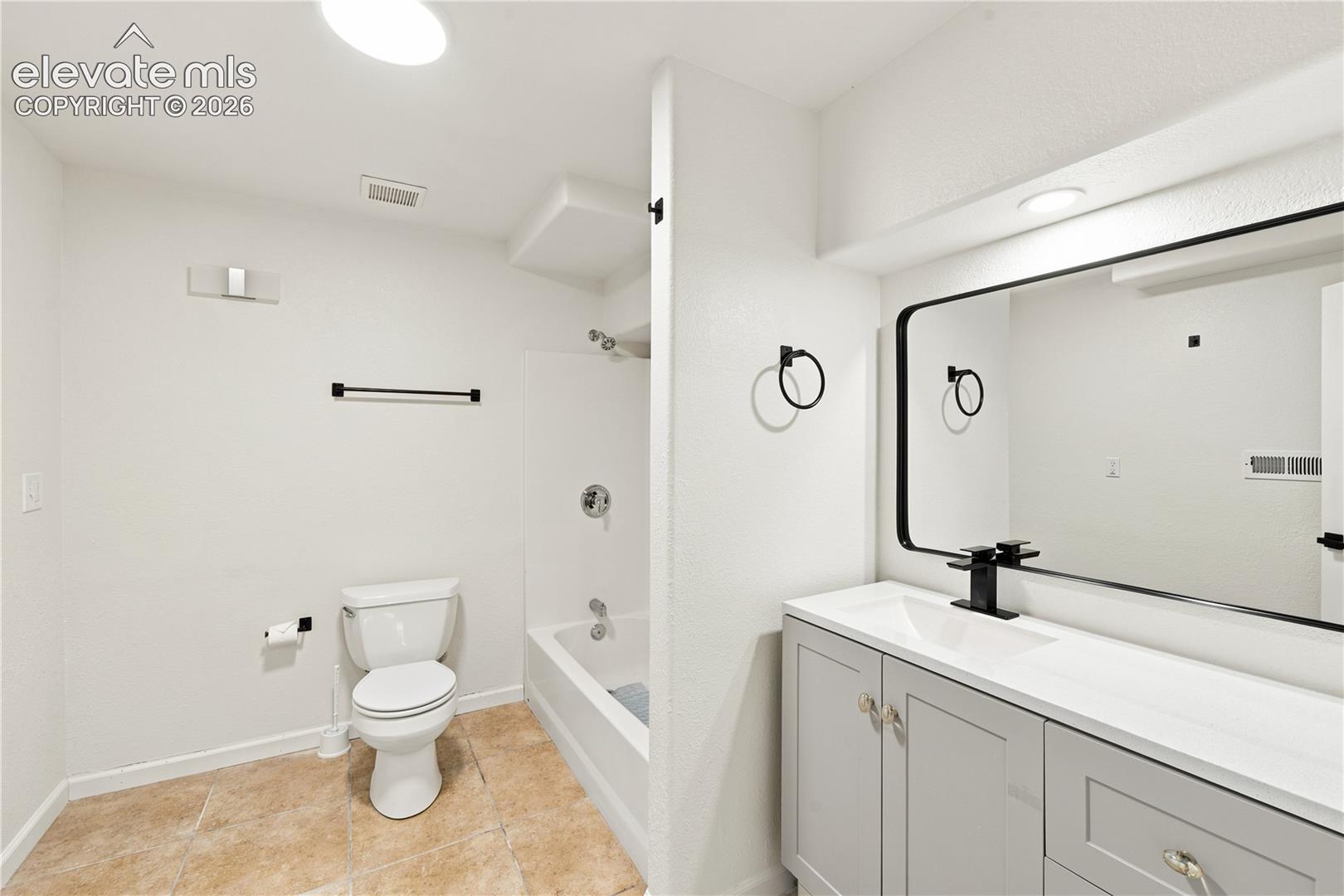 Contemporary bathroom featuring a light gray vanity with a white countertop and an integrated sink, complemented by a large framed mirror with a matte black finish