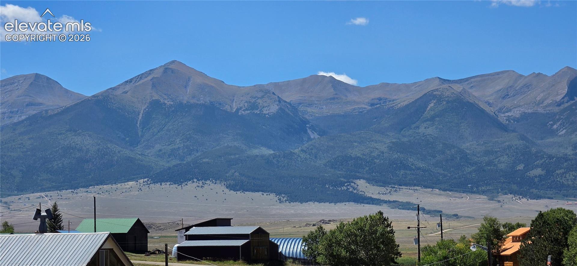 Expansive mountain range backdrop with distant foothills, scattered trees, and a clear sky